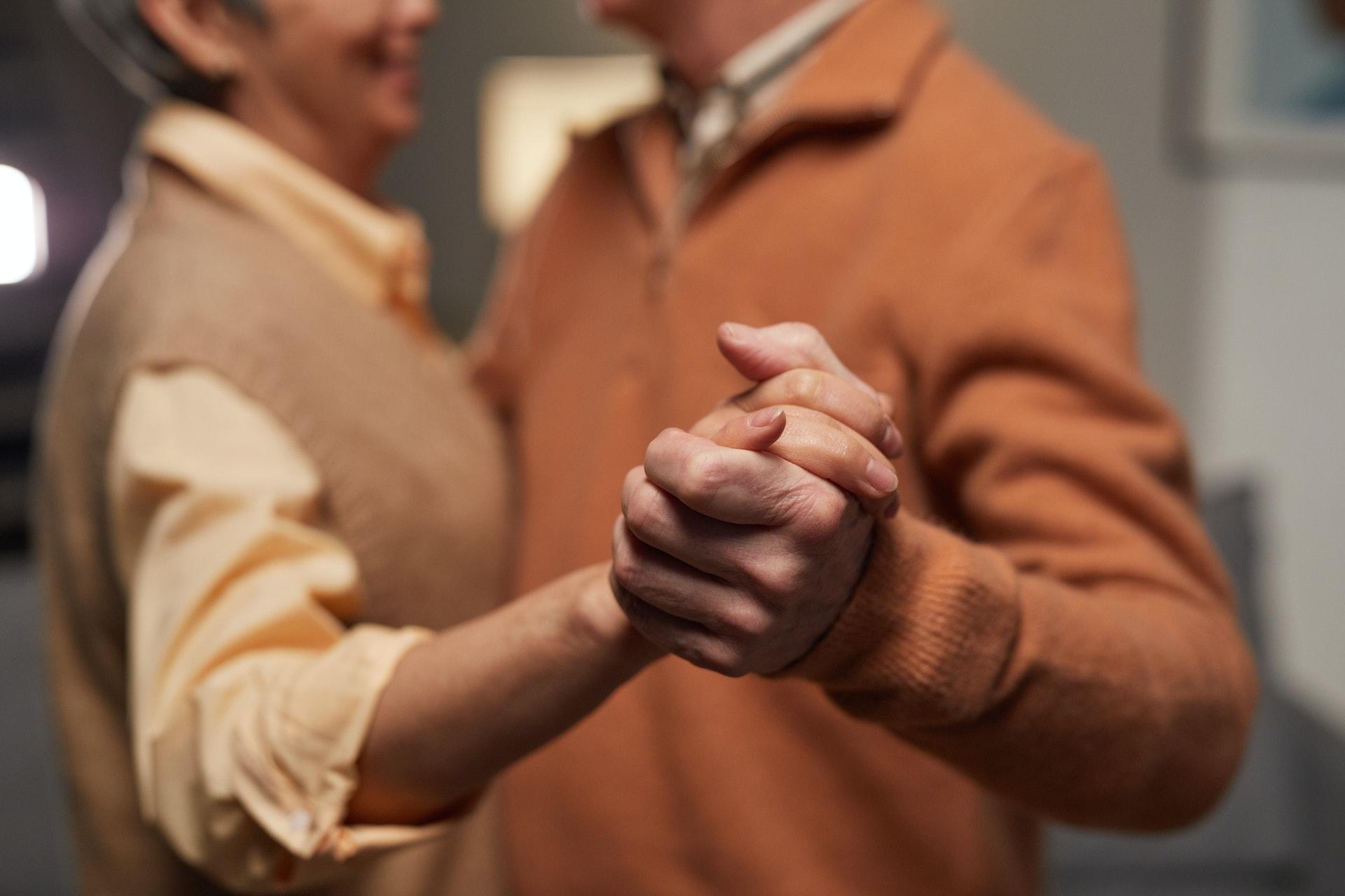 An elderly couple holding hands and dancing together.