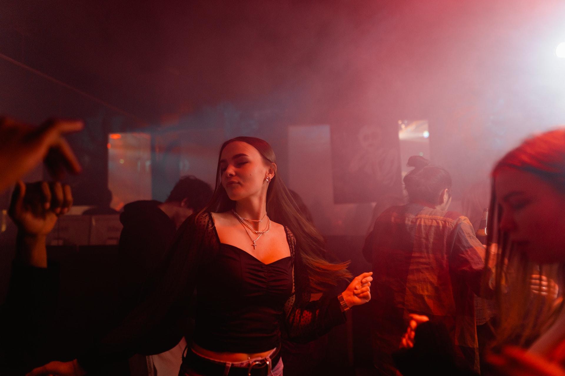A teen dances at a club with red lights and mist.