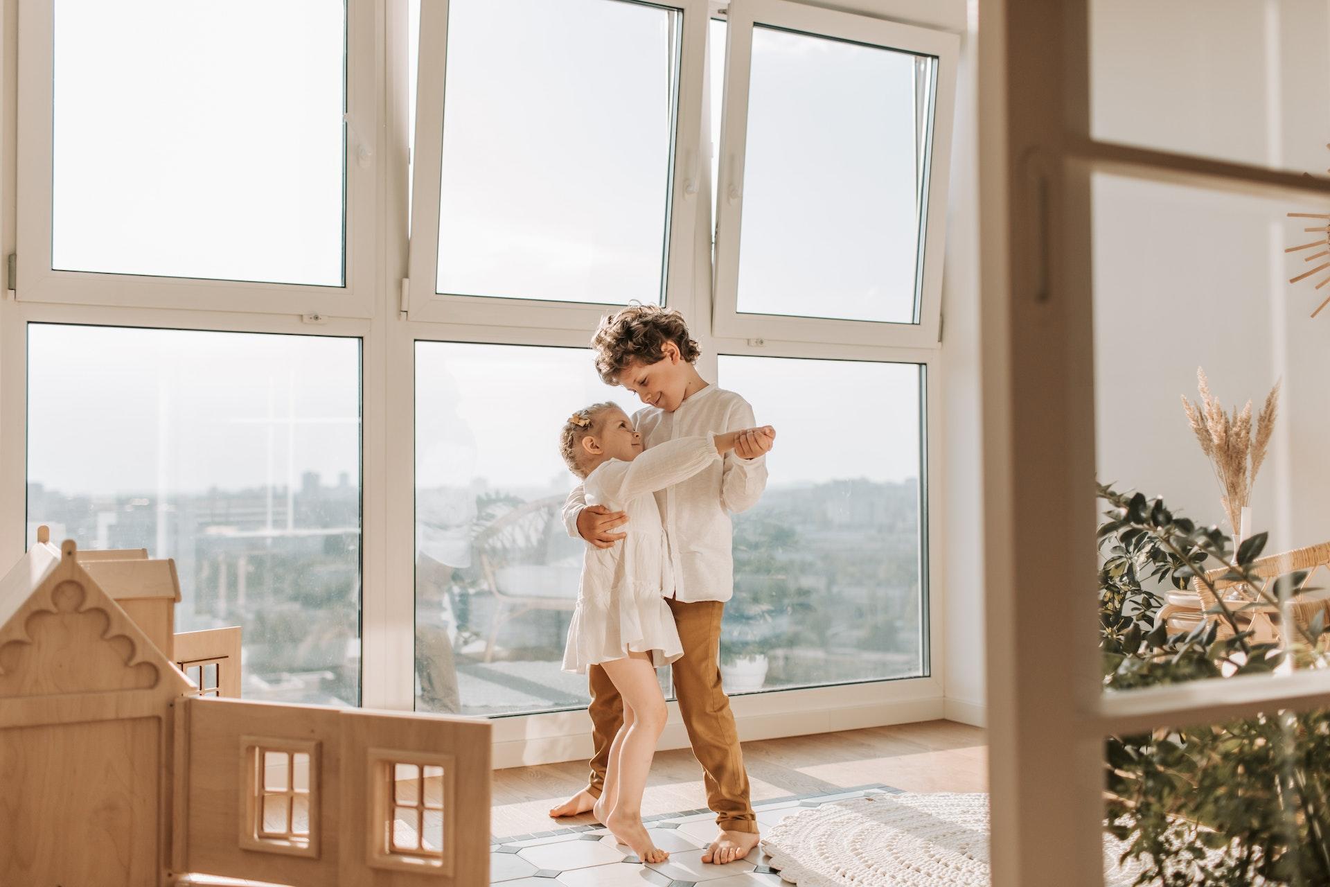 Two young siblings dancing together in a sunny room.