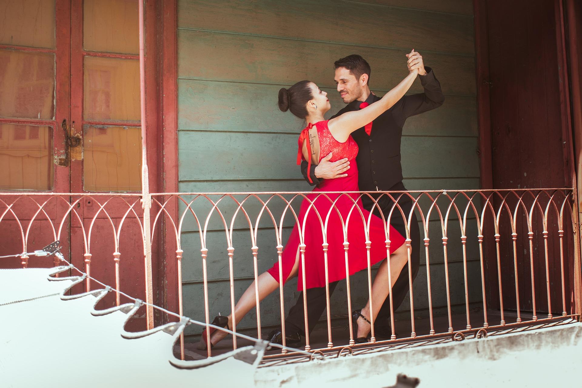 A couple dances on a balcony together in fine clothes.