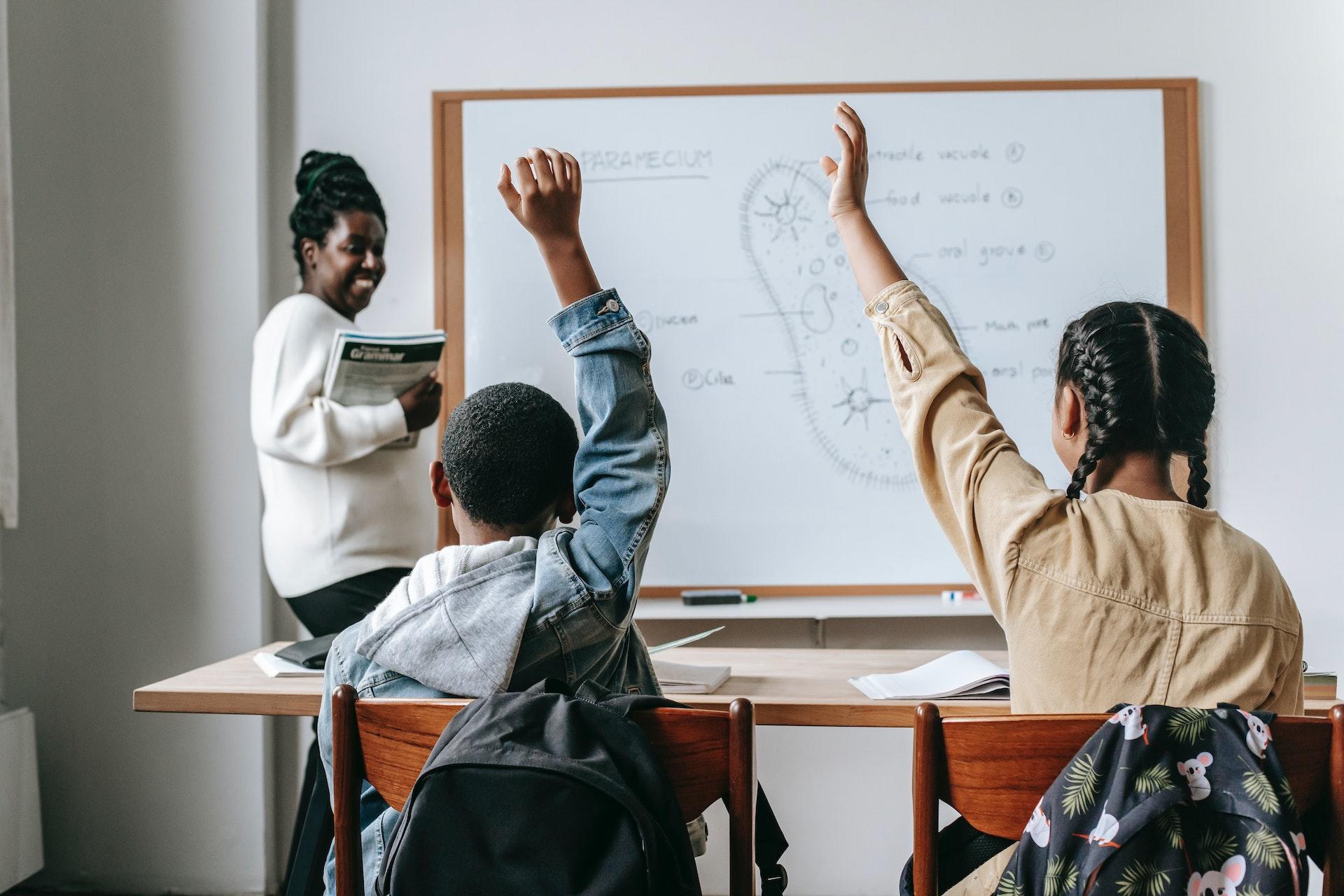 A middle school teacher stands at the front of the class. A paramecium is drawn on the whiteboard.