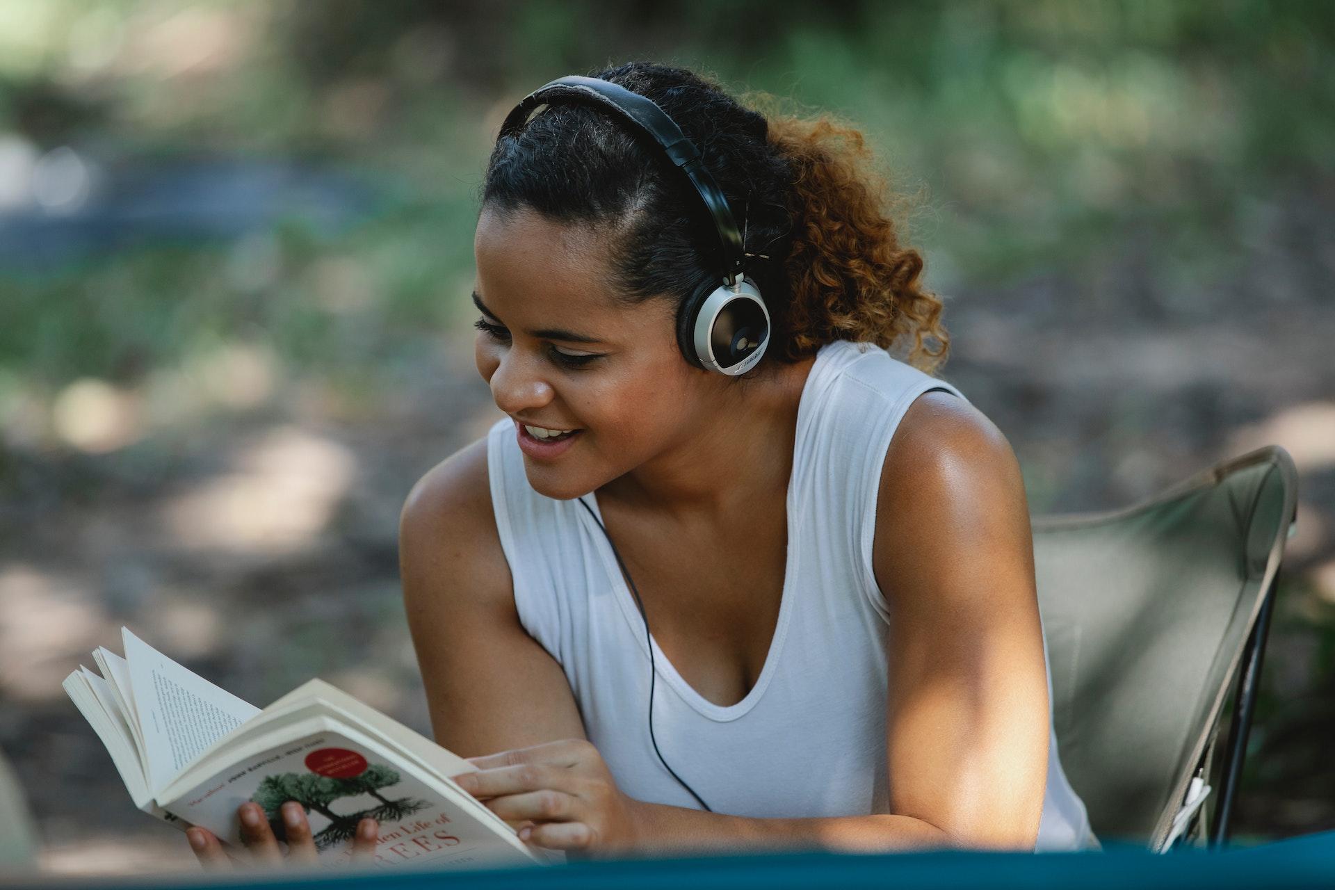 A woman listening to music or a book with her headphones while reading.