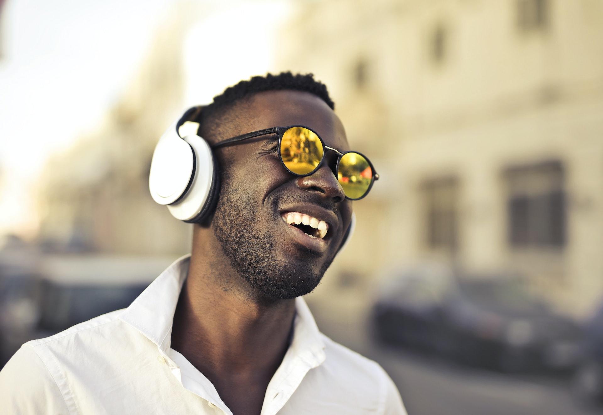 A man wearing headphones and reflective sunglasses smiling.