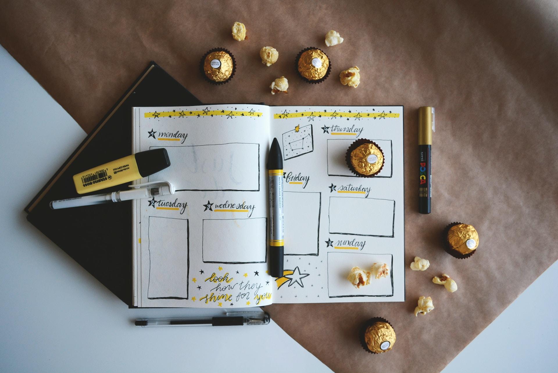 A planner written in black and yellow with chocolates nearby.