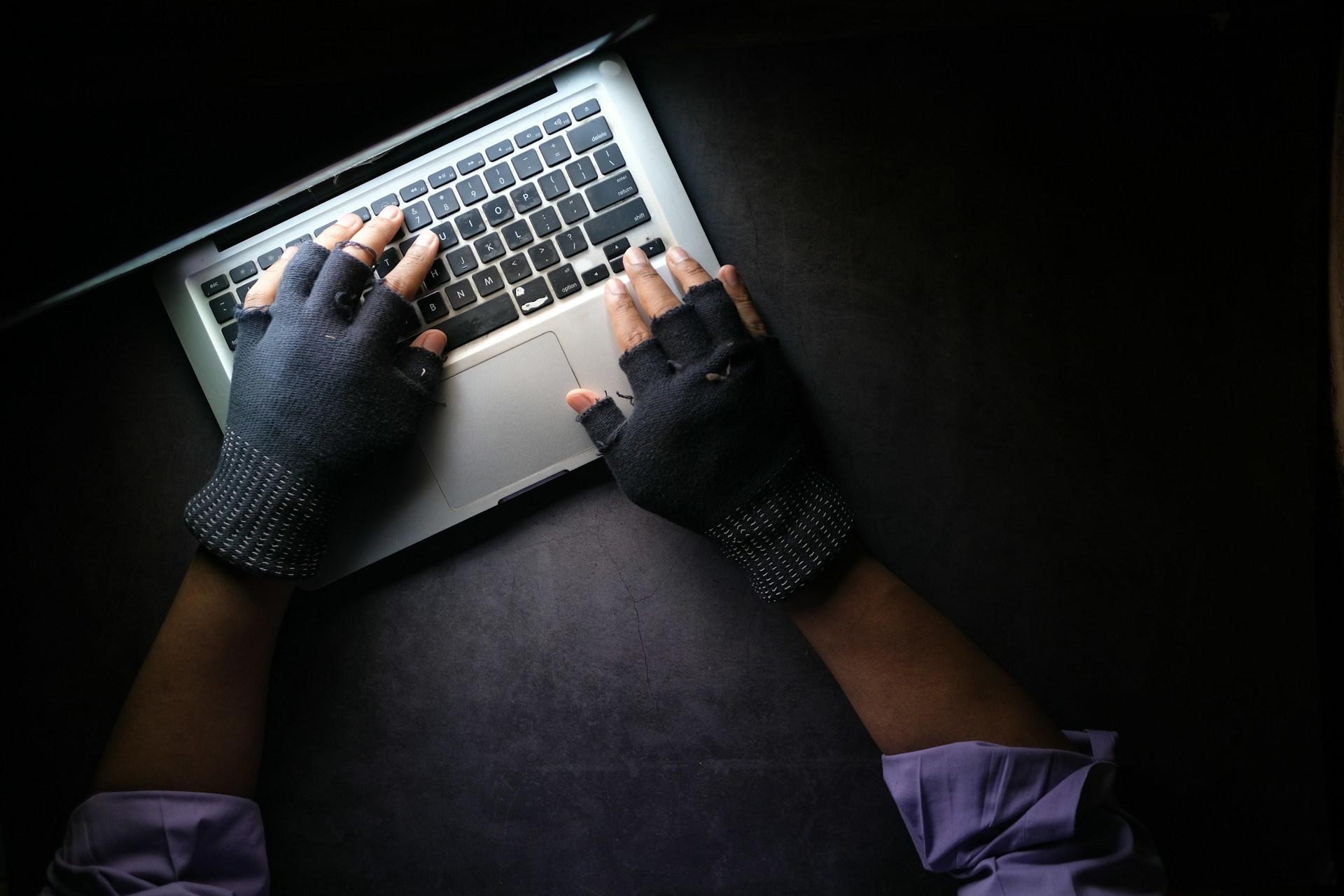 A pair of hands wearing gloves and typing on the computer