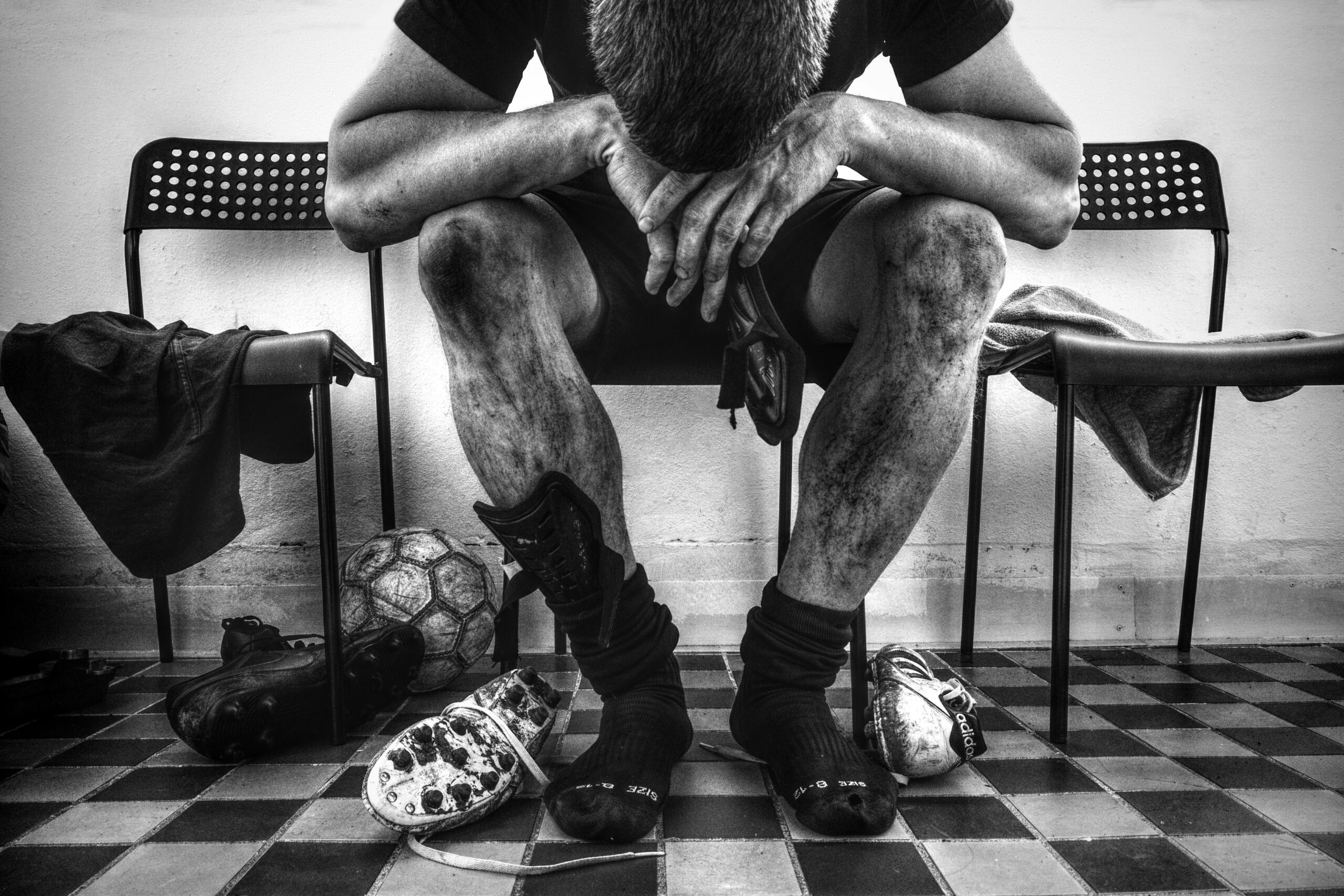 A man sitting on a chair, looking down with a disappointed expression after a loss.