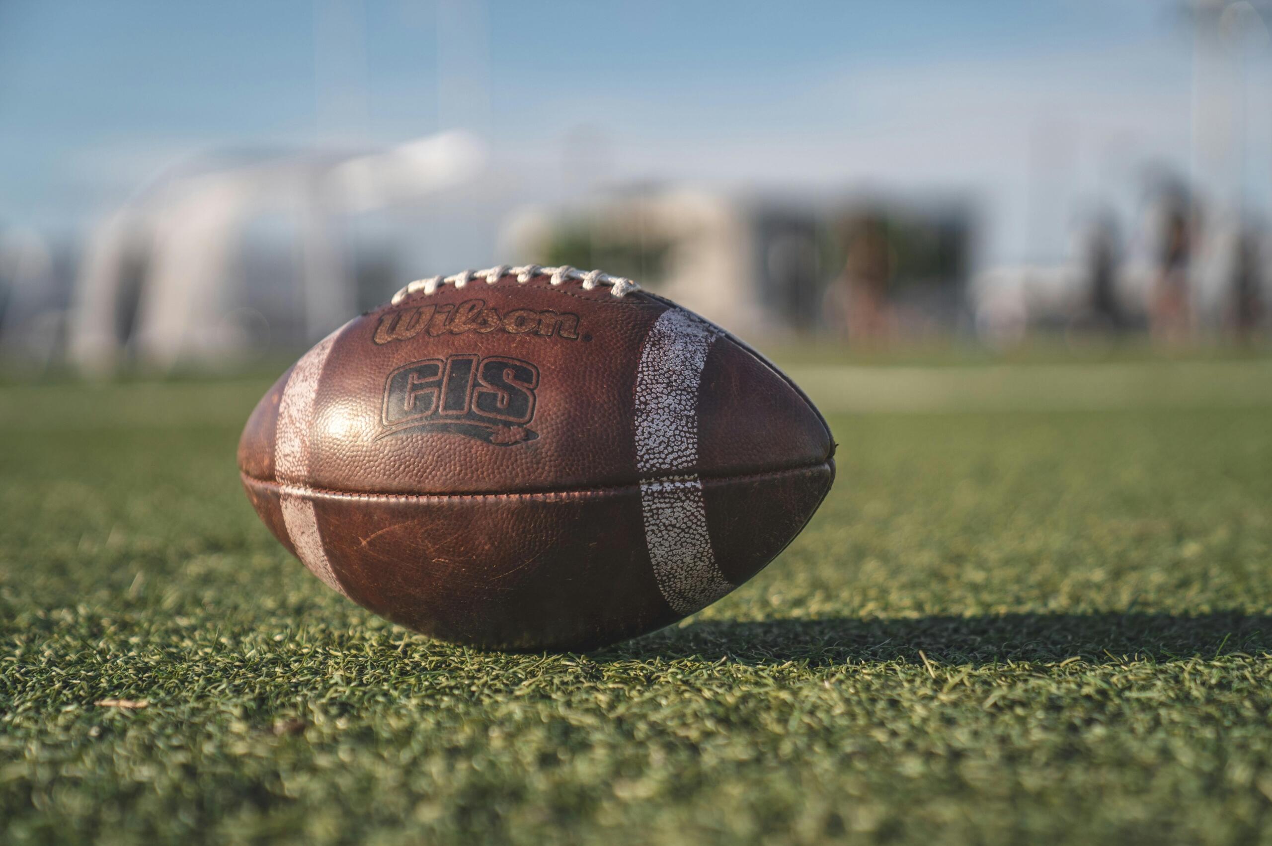 Close-up of a brown Wilson pigskin football on green grass, with selective focus.