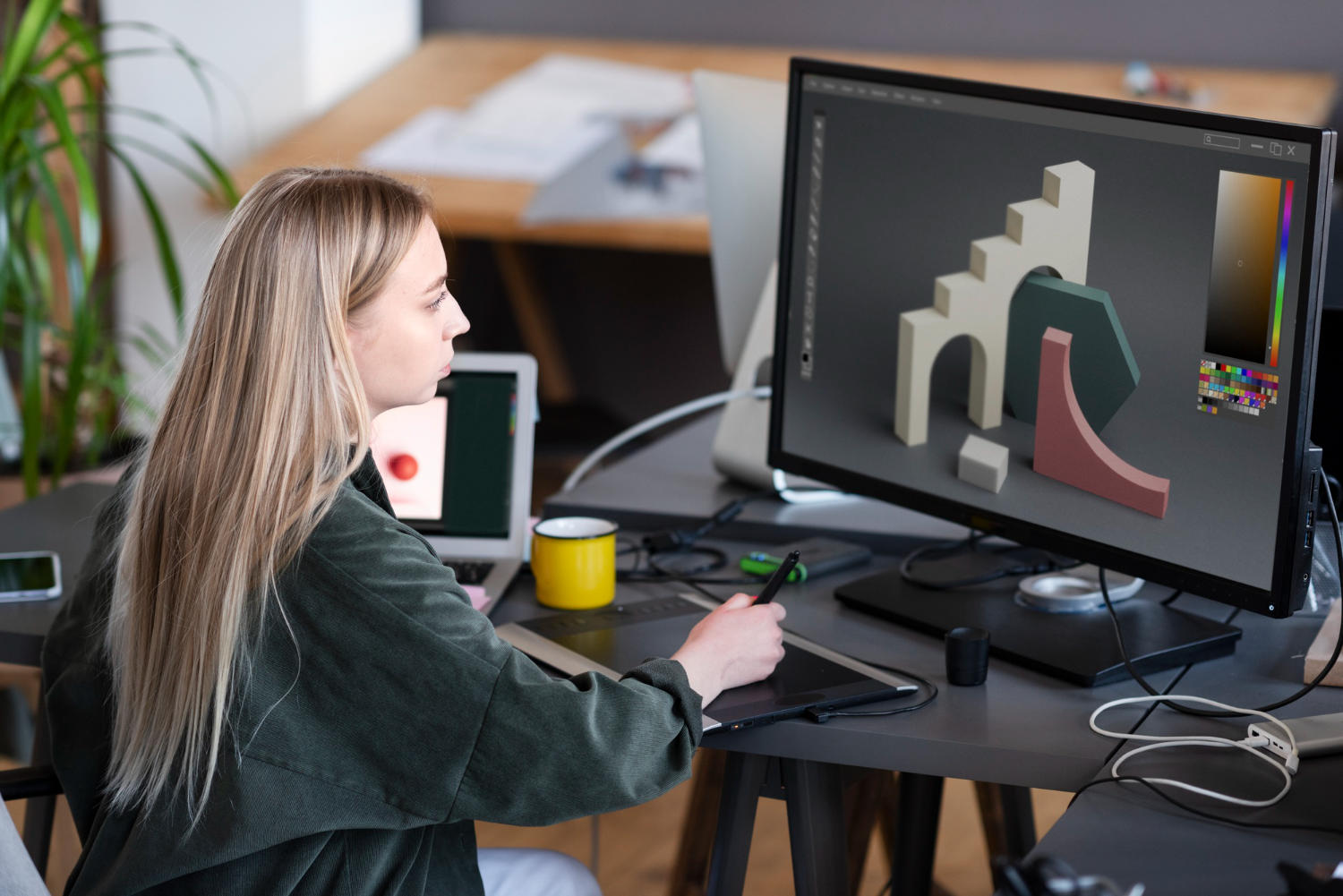 A 3d artist creates a 3d scene on a computer using a graphics tablet.