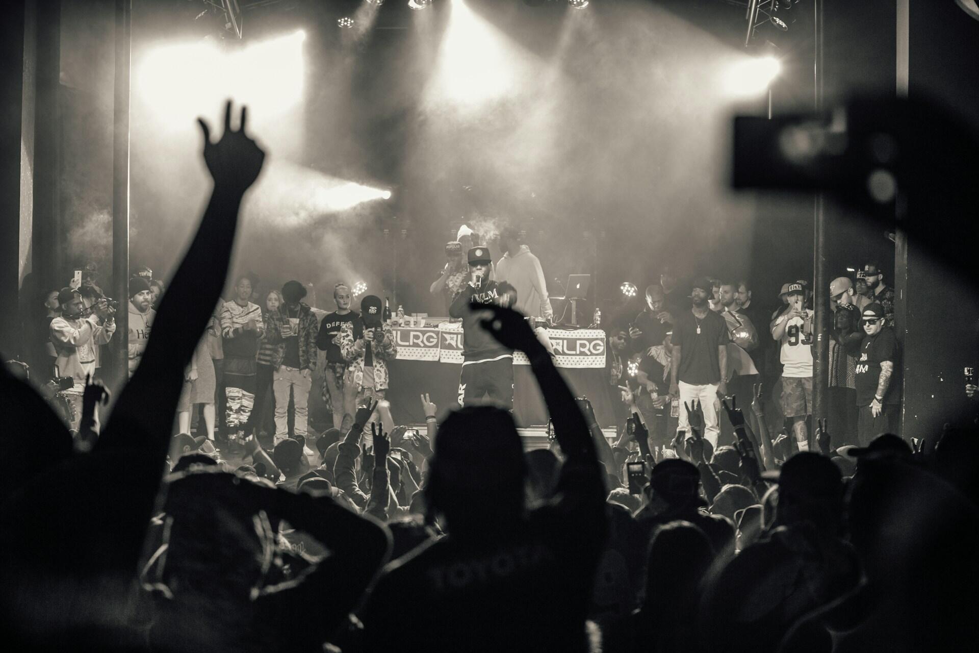 A rapper performing on stand in front of fans raising their arms.