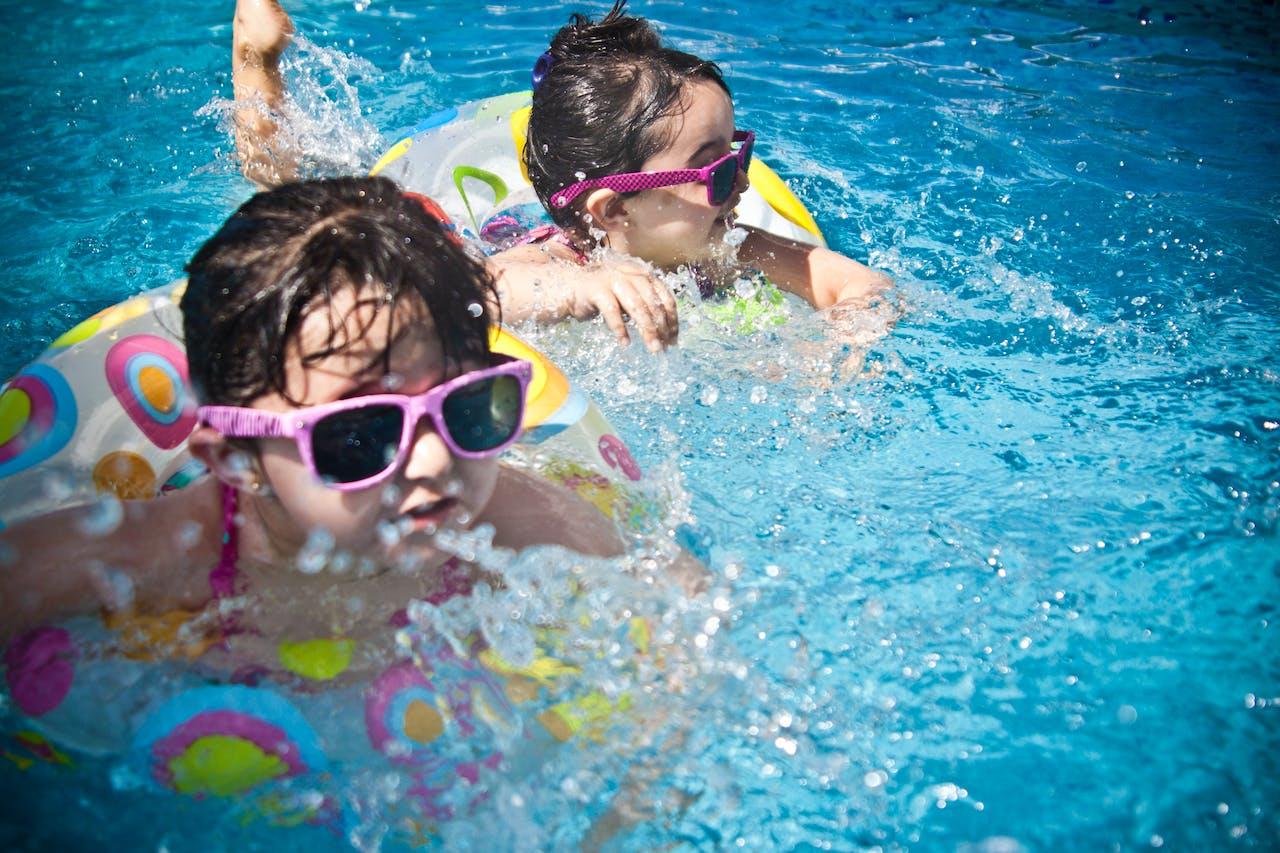 Two kids in floaty rings wearing sunglasses and splashing in the pool.