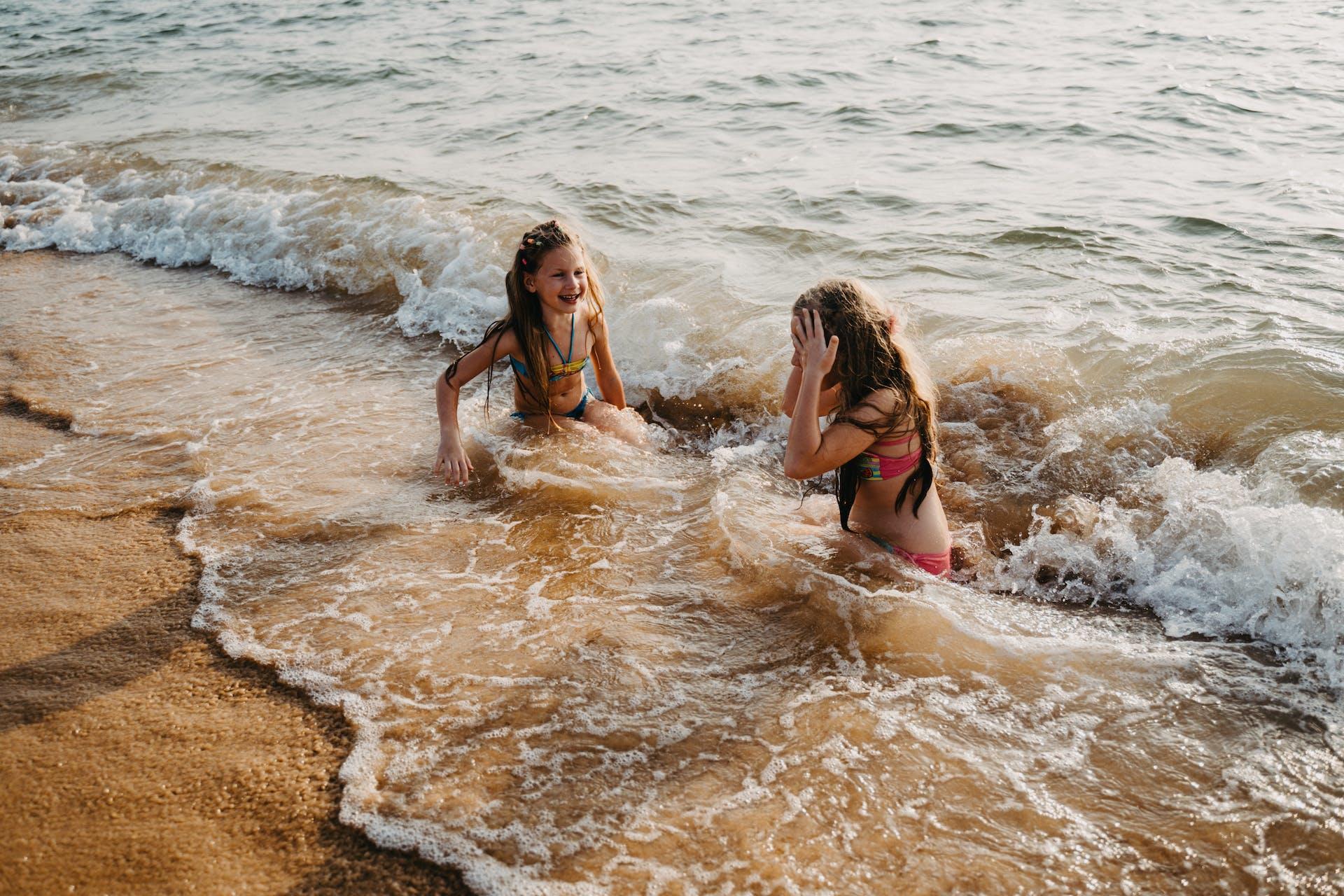 Young kids sitting in the swash of water at the beach.