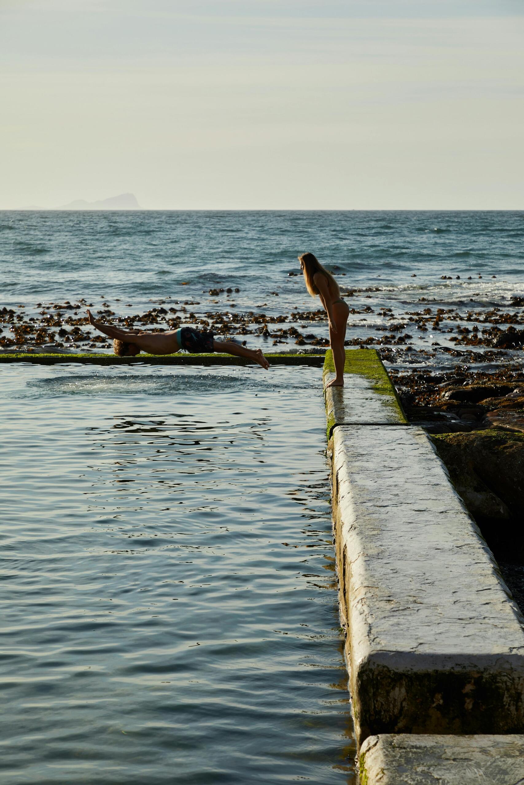 A man and a woman swimming in a tidal pool, surrounded by natural rocks and calm water.