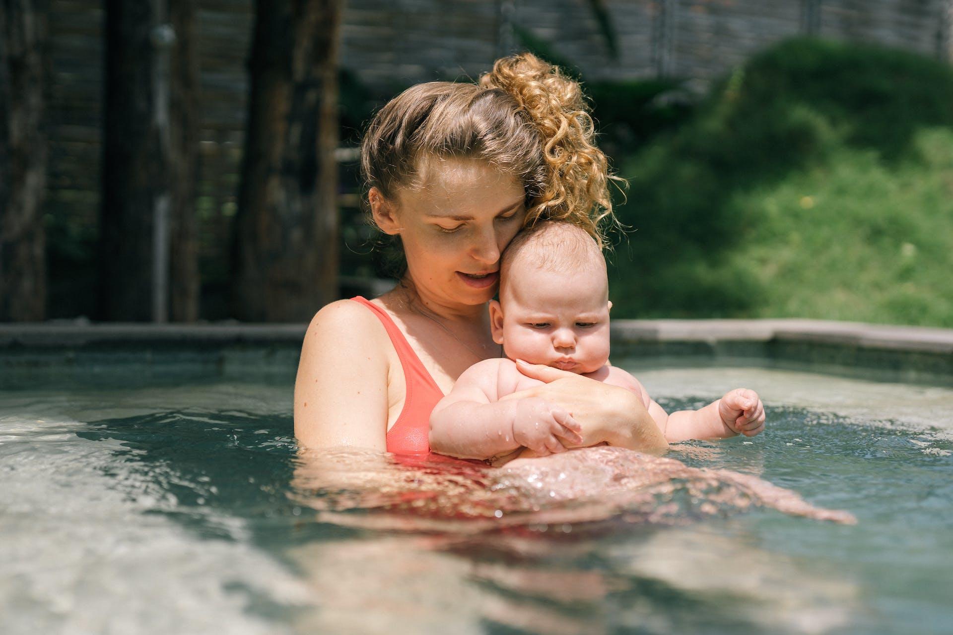 A mother holds her baby in a swimming pool.