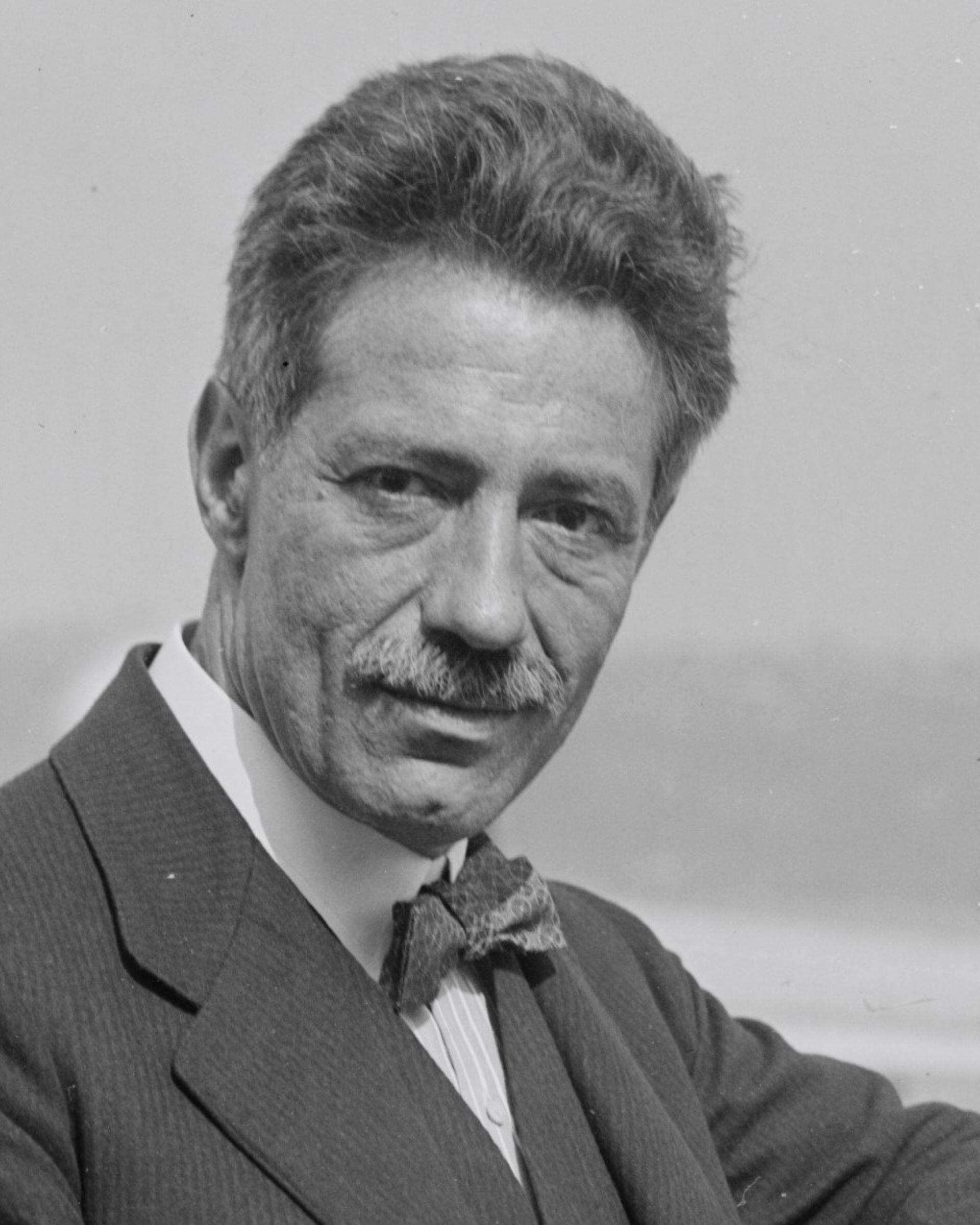 Black and white portrait of a man with a moustache playing the violin in formal clothing.