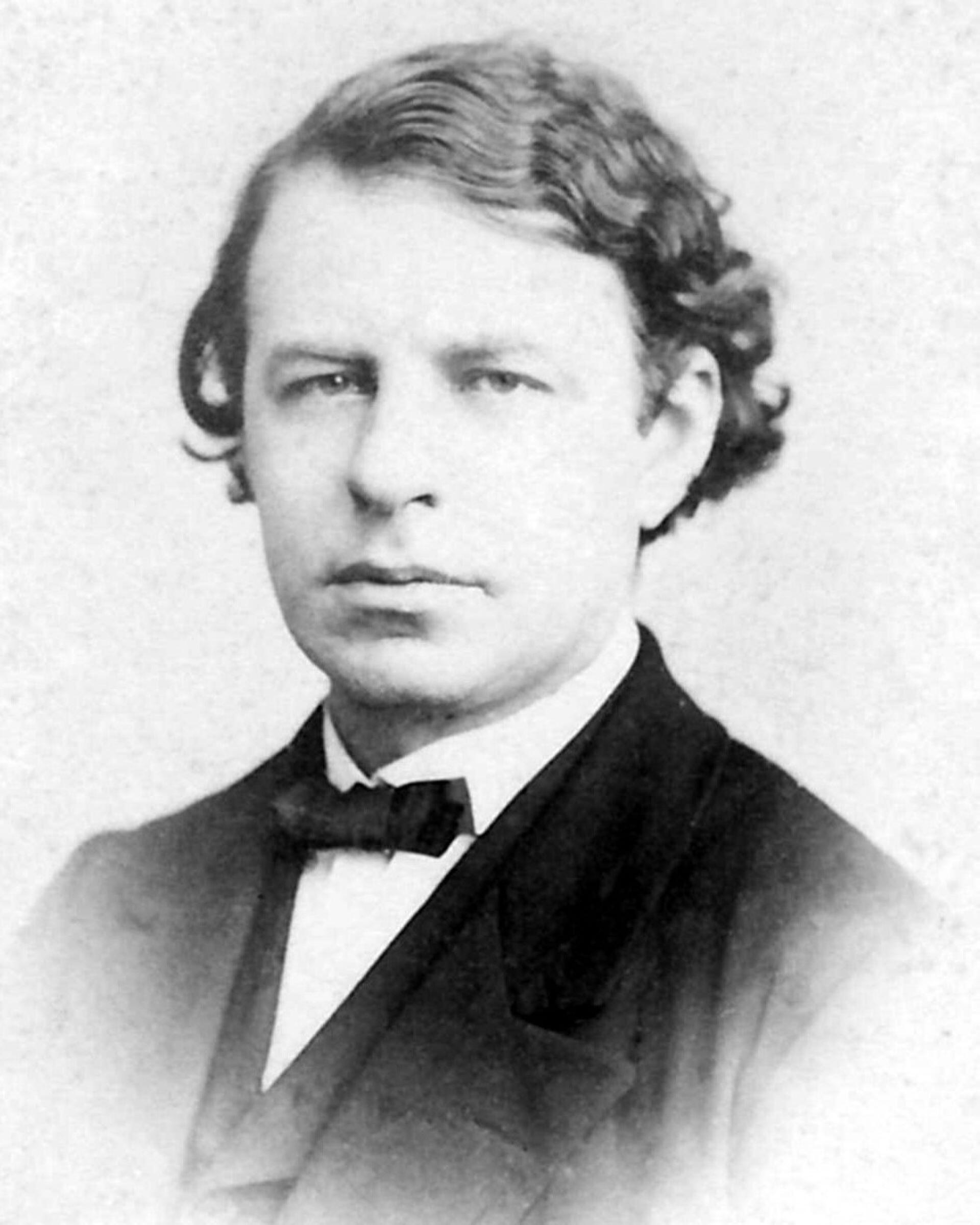 Black and white portrait of a man in formal attire with arms crossed, looking to the side.