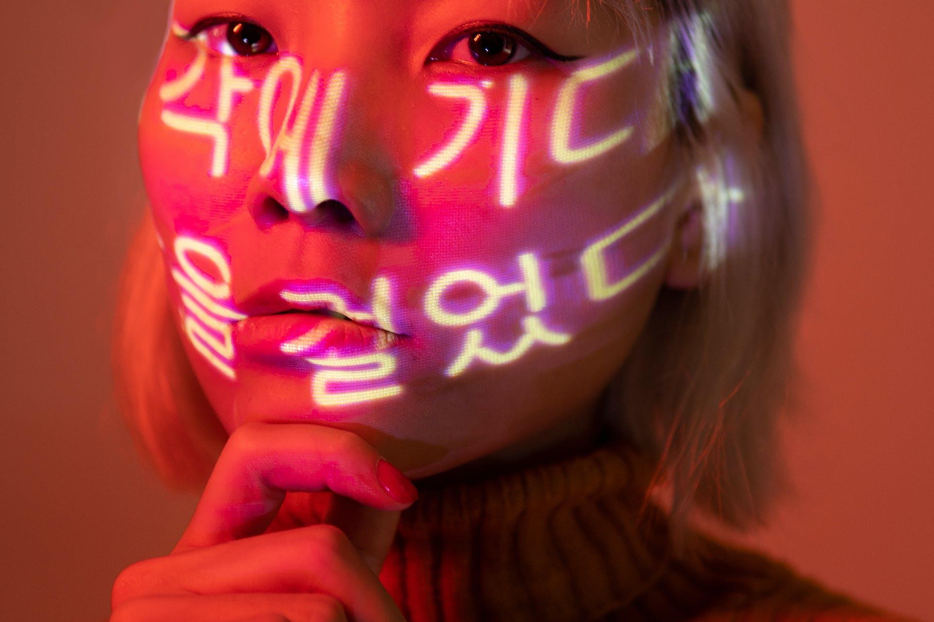 The woman's face is brightened by a light with Korean characters printed on it.