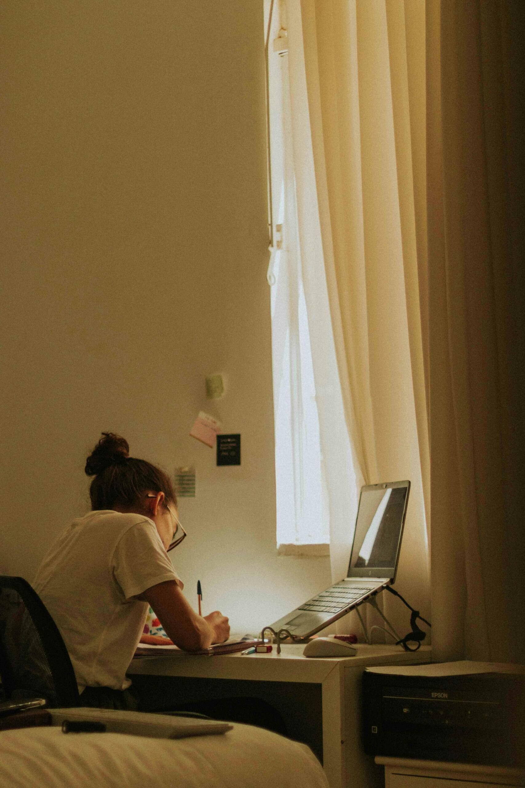  Young woman studying beside a window with soft natural light illuminating her workspace.