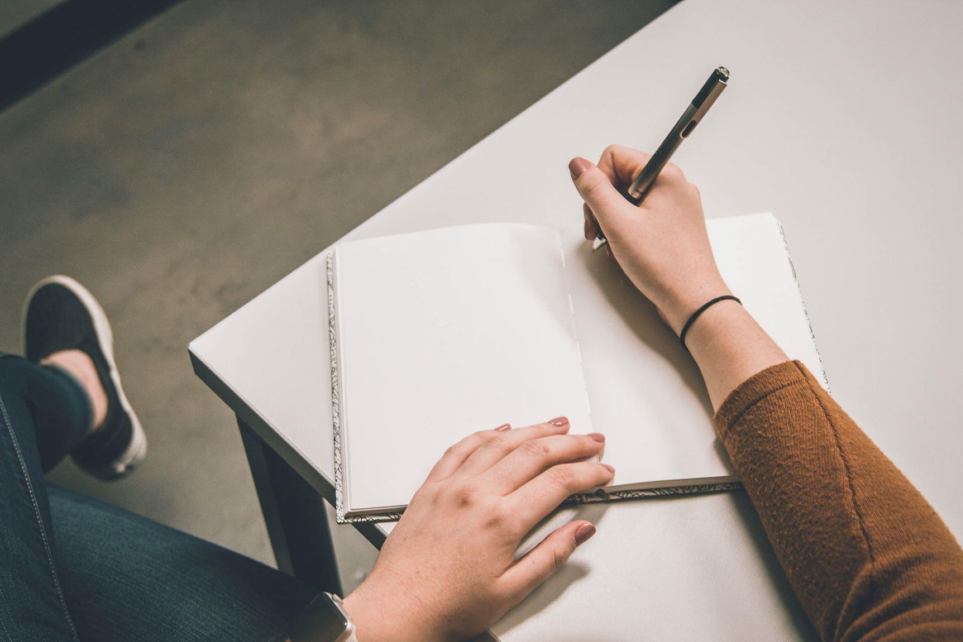A person sitting at a table with a notebook and a pen.