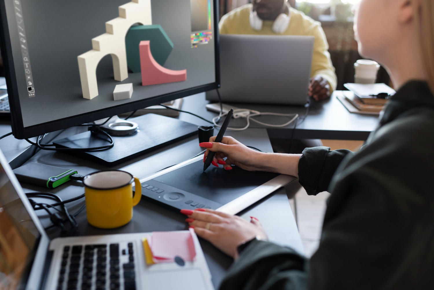 A 3D modeling artist making a model on the computer using a pen tablet and desktop computer.