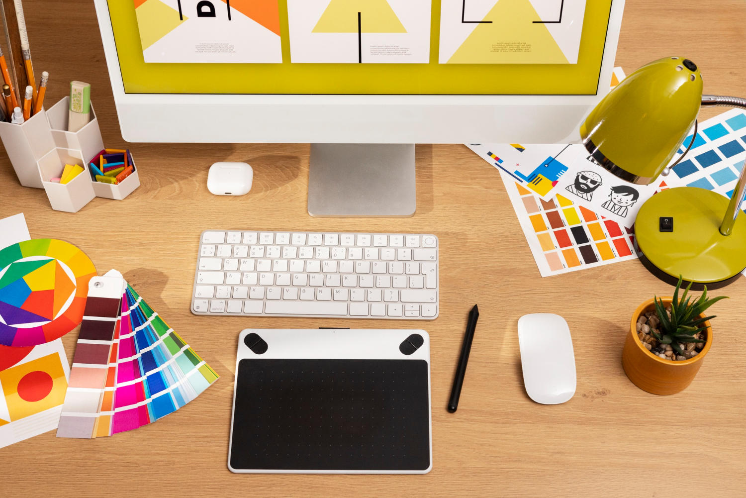 Desk with pen tablet and desktop computer with color reference sheets nearby.