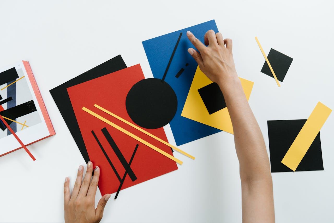 A top-down view of a person rearranging paper cut into various shapes, experimenting with design