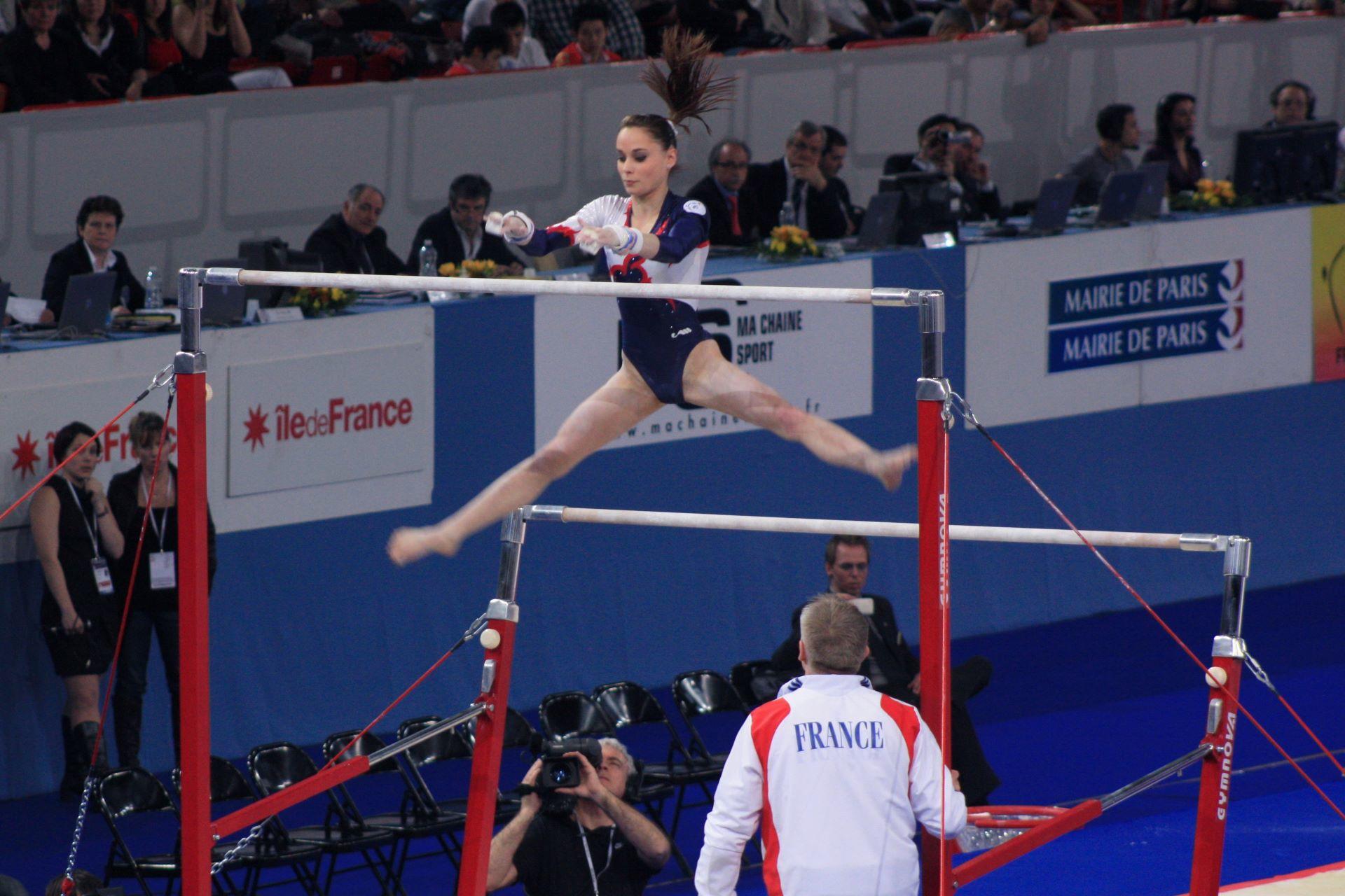 A gymnast mid-air during a release in an uneven bars routine.