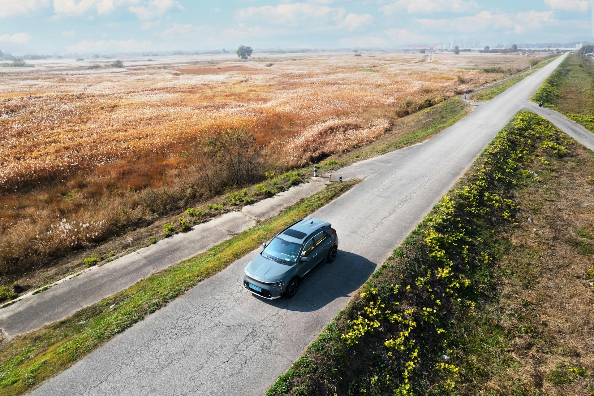 A photo of a car driving on a road with golden fields on one side and green grass on the other