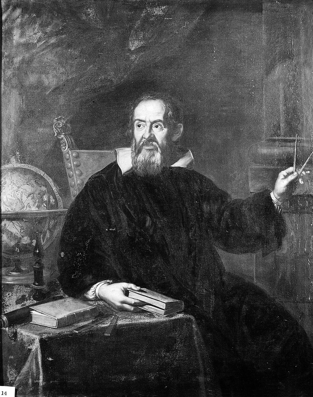 An image of Galileo Galilei wearing a black robe, sitting down in front of a table;