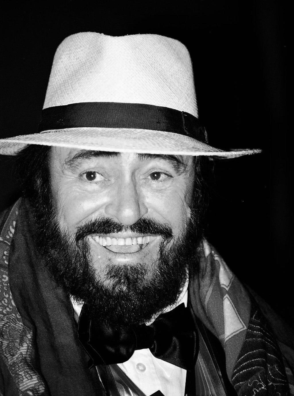 Luciano Pavarotti in a white hat, wearing a suit and bow tie.