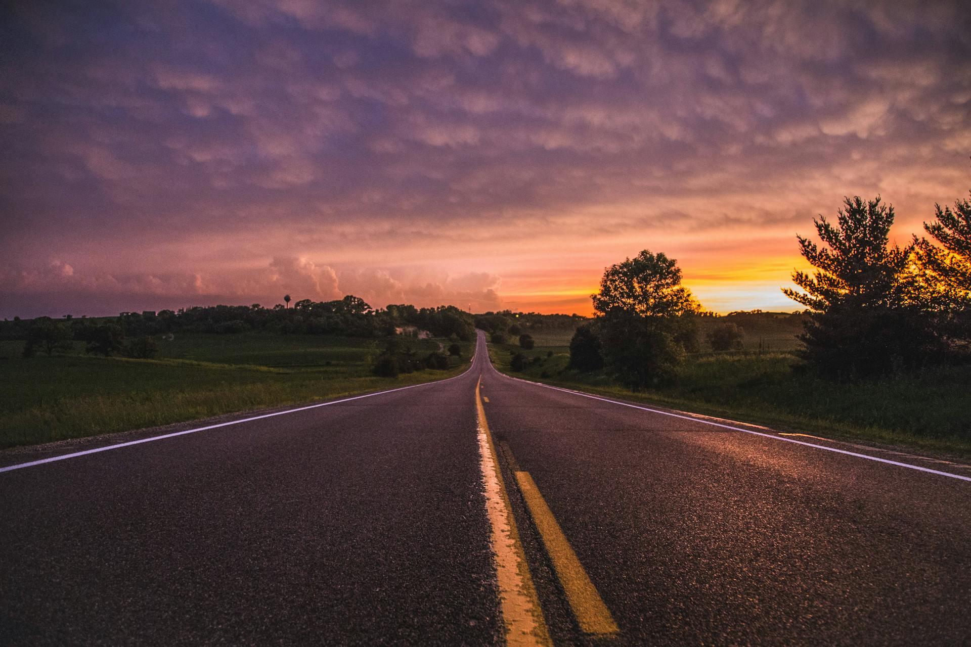 A road stretching into the distance in a grassy area at sunset