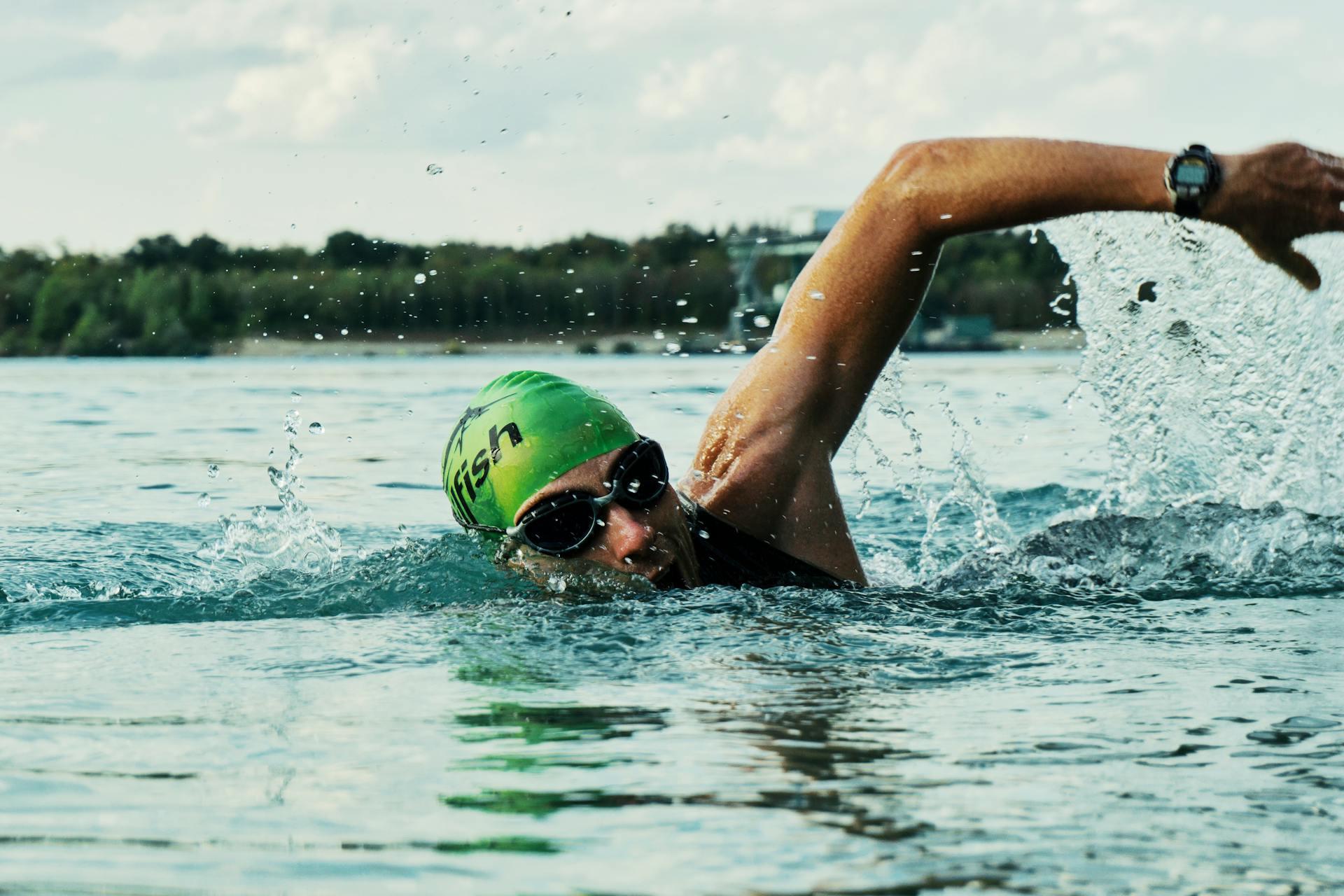 Someone swimming in a lake with a green swim cap on and googles.
