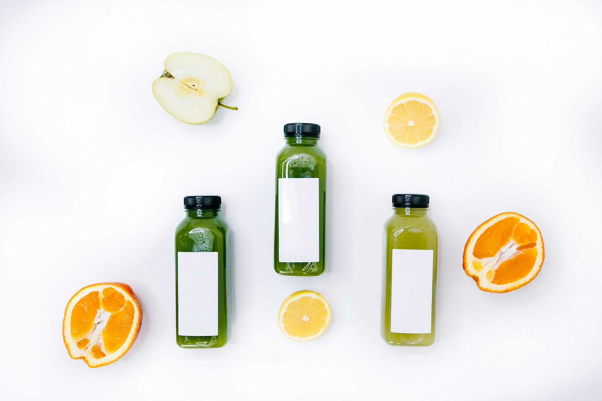 Three green juices with an apple, orange, and lemon cut next to them.