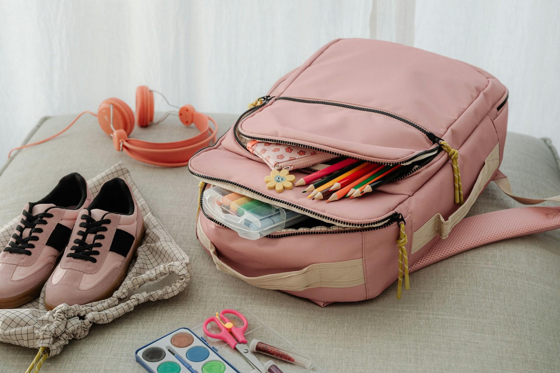 Pink shoes and a pink backpack with back to school supplies.