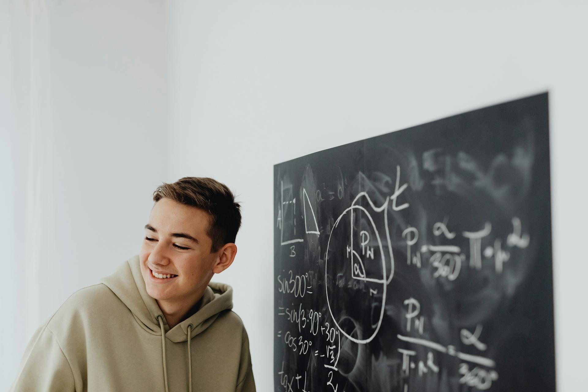 A student smiling near a chalkboard with lots of math and algebra equations written on it