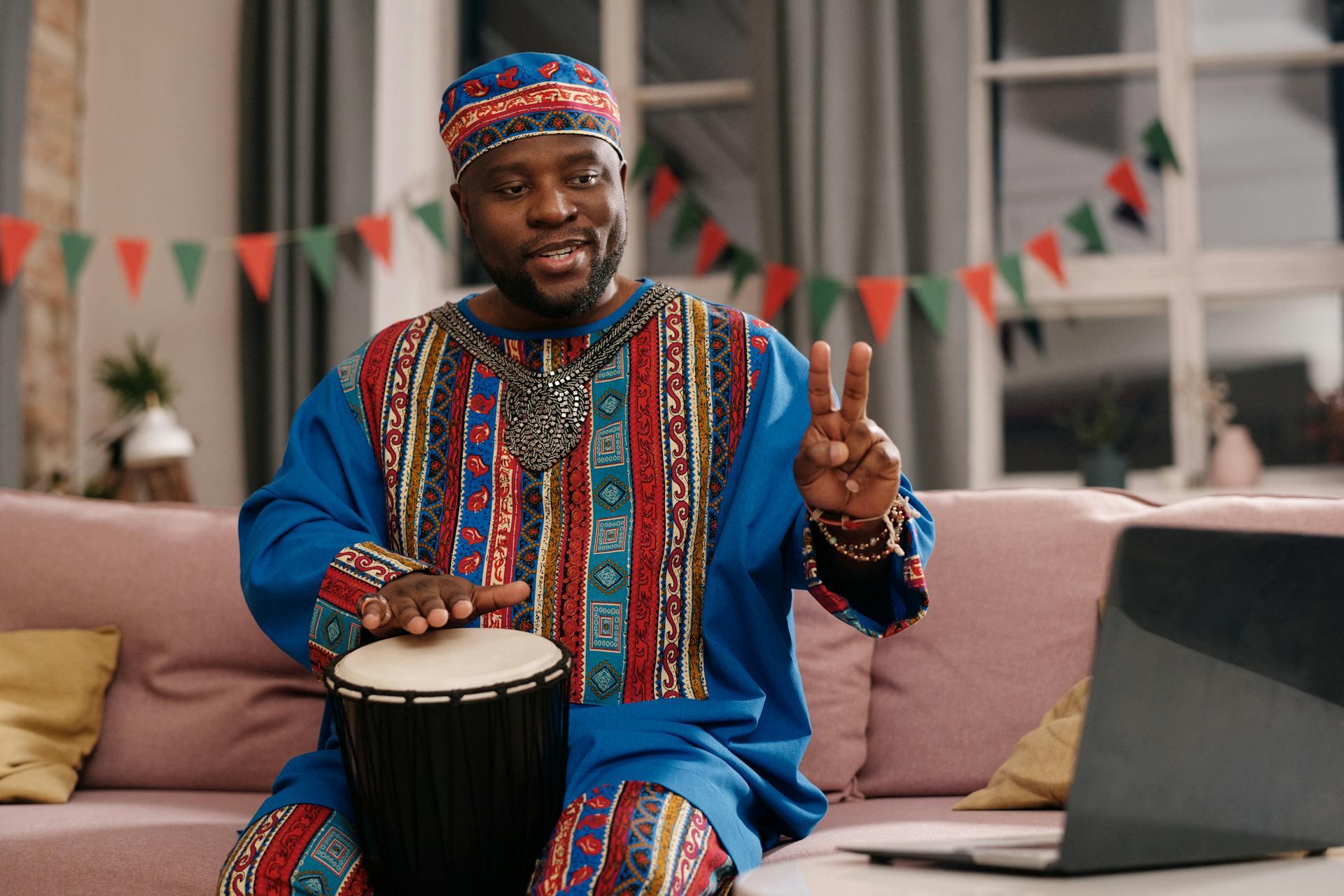 A man wearing a traditional dashiki shirt, holding a hand drum.
