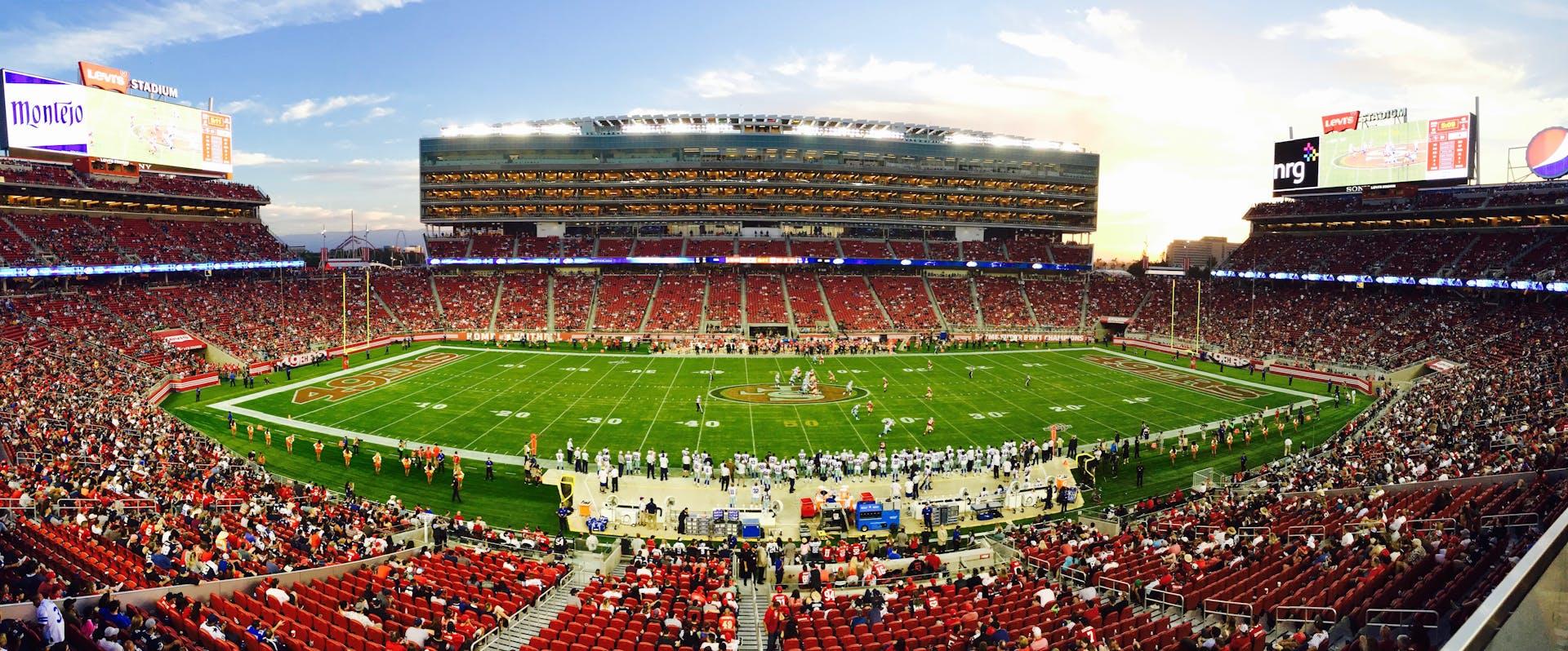 A wide hot of a football stadium, showing lots of fans and players getting ready to start the game