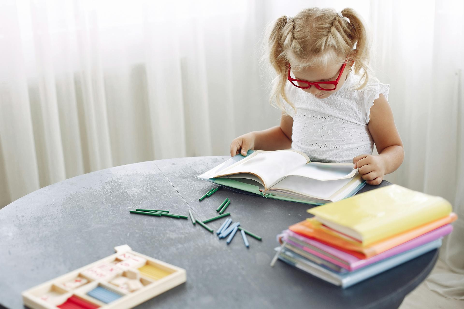A young girl with red glasses reading at the table.