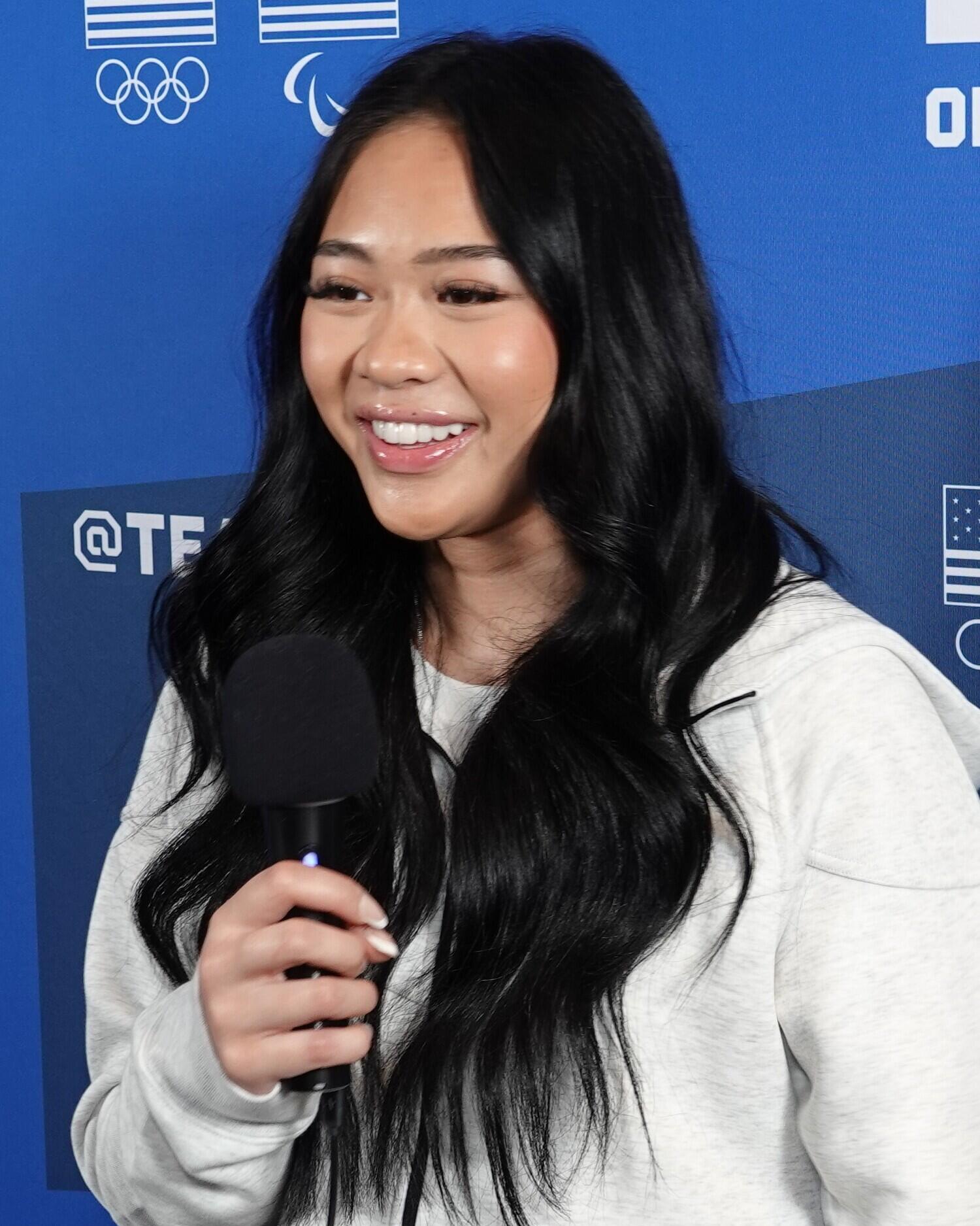Suni Lee in front of a blue background, holding a microphone.