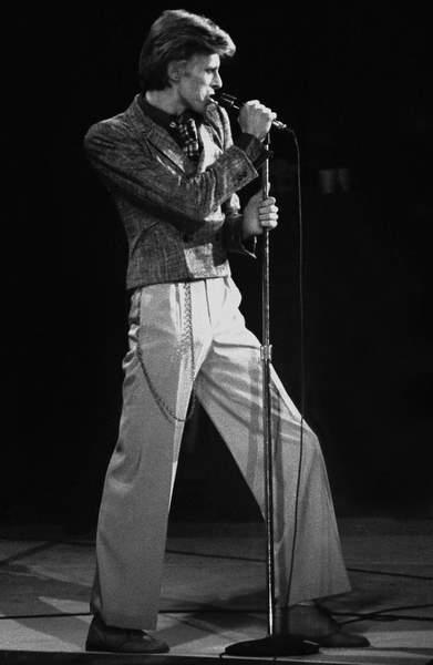 a black and white photo of Bowie singing with a microphone on stage