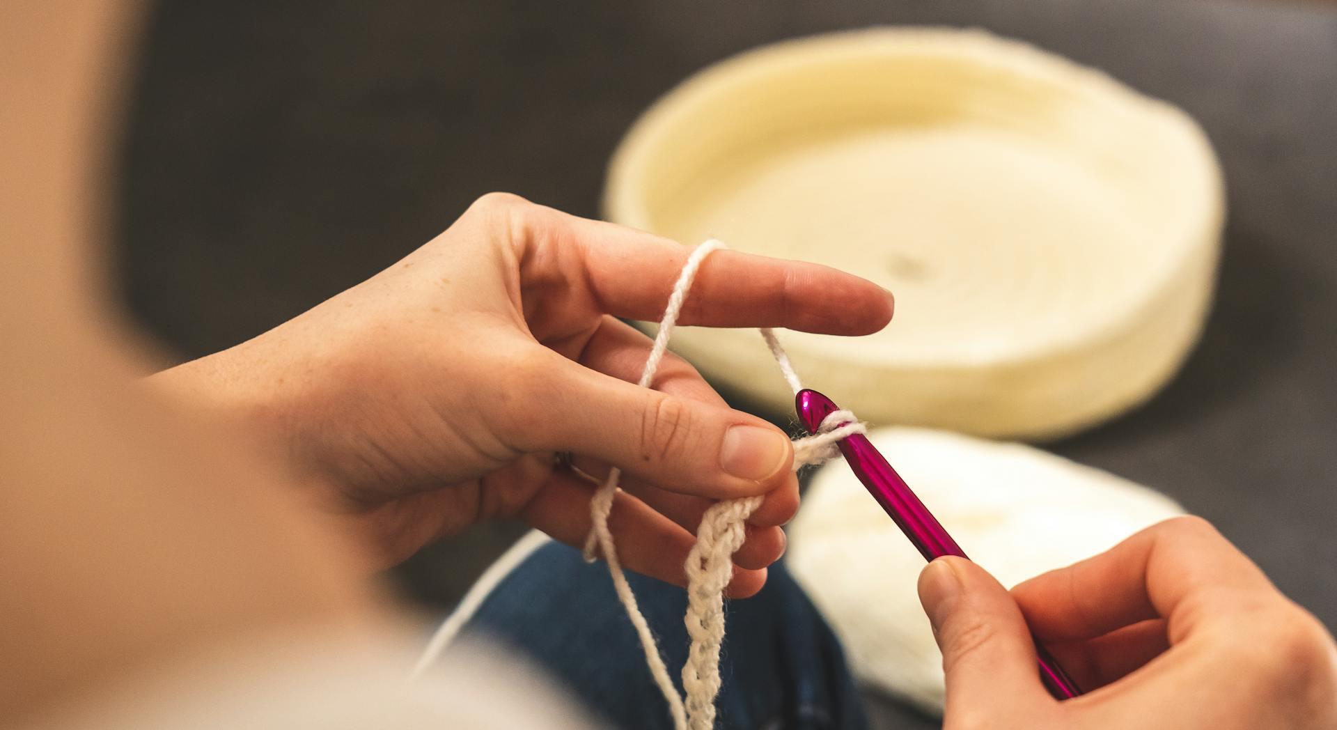 A person crocheting with a pink hook and cream colored yarn