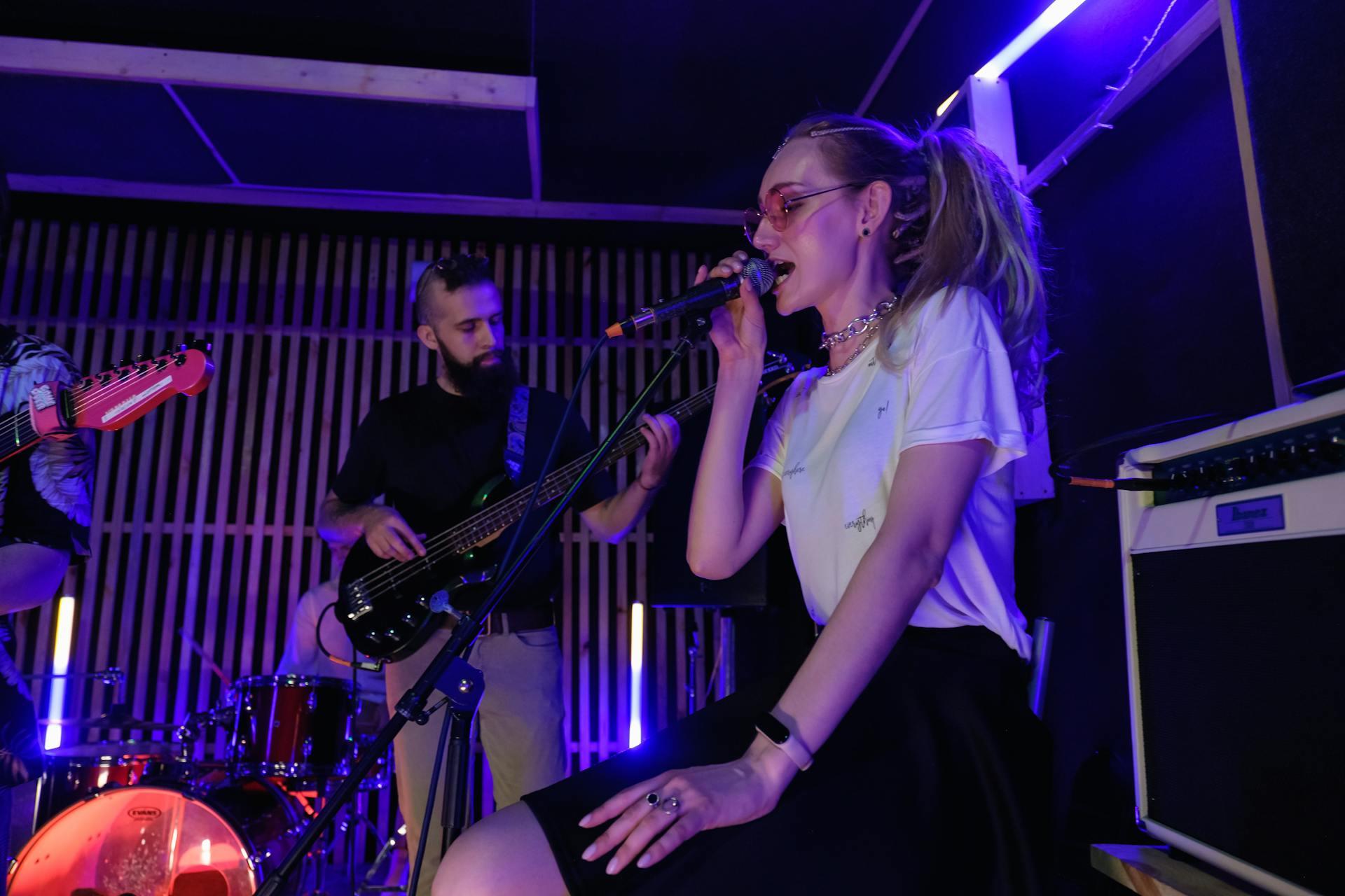 A woman in a white shirt singing into a microphone with backup musicians and blue lights around