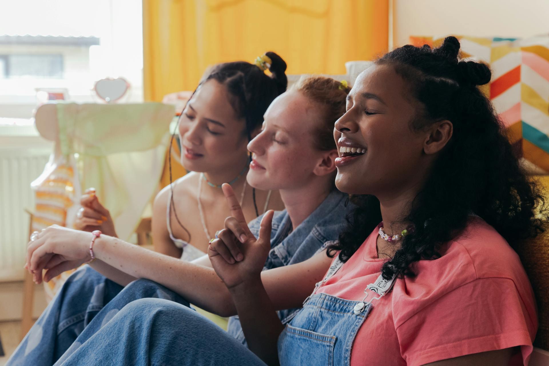 A group of three young females singing while sitting on the floor.