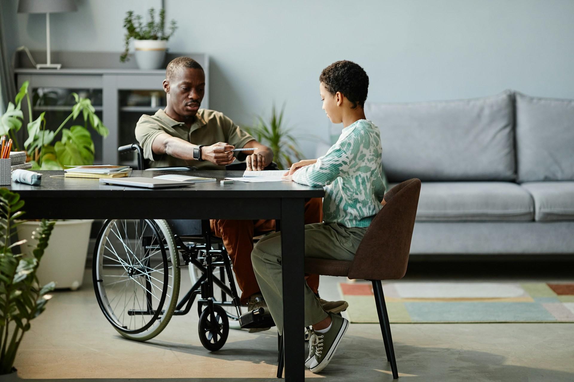 A tutor in a wheelchair and a student sitting at a table.