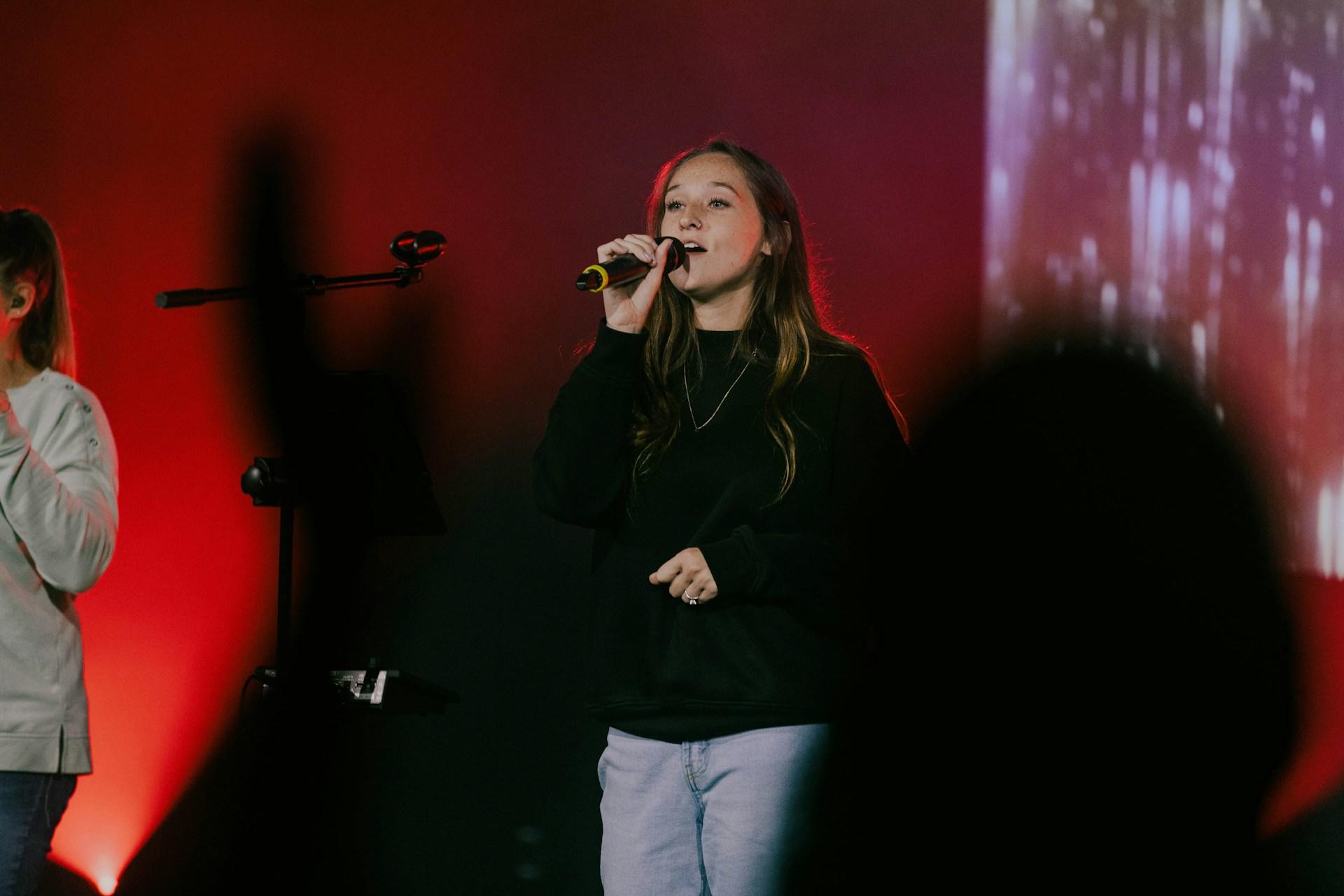 A woman singing into a handheld wireless microphone on stage.