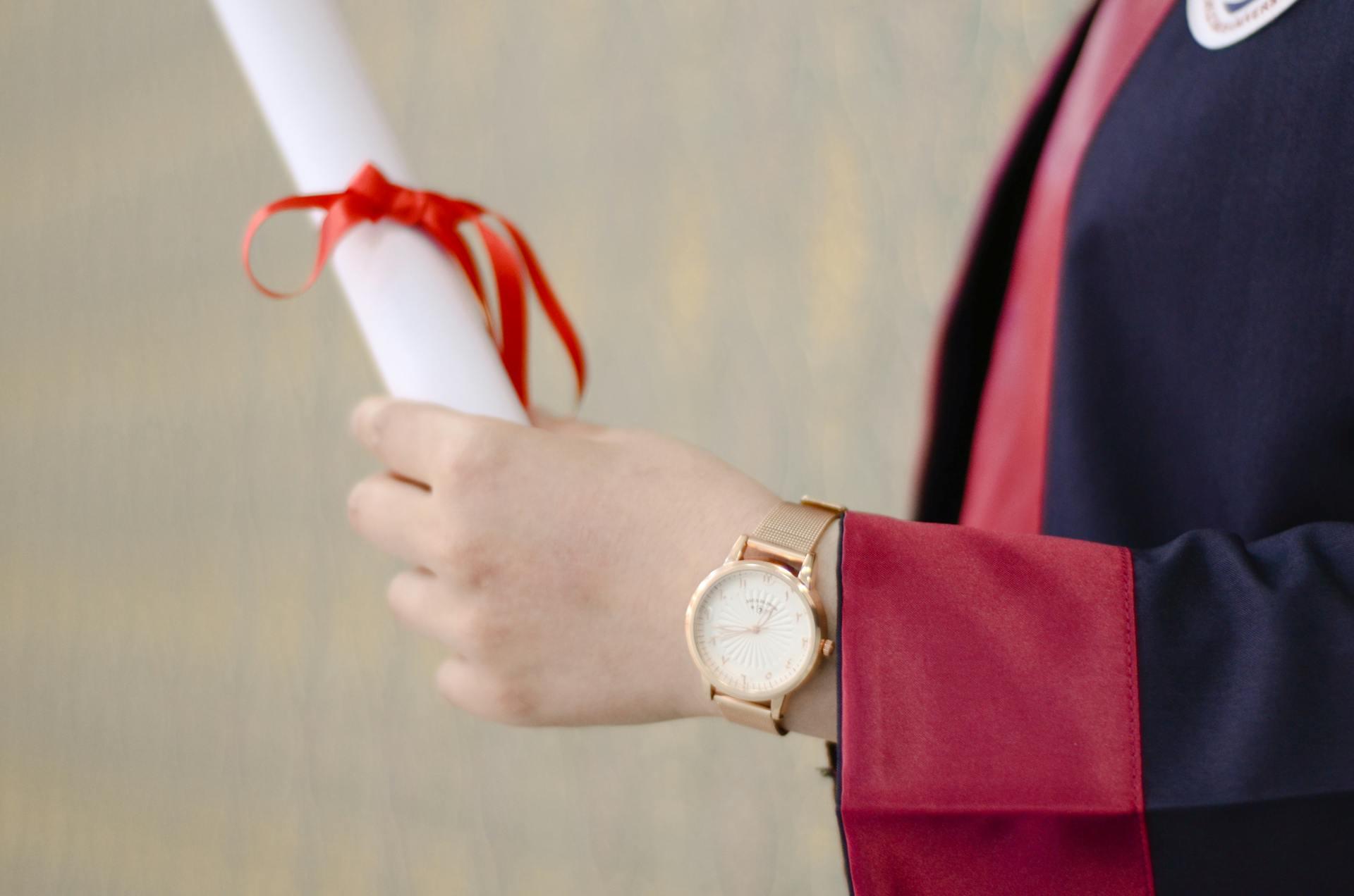 A man holding a diploma wearing graduation garments