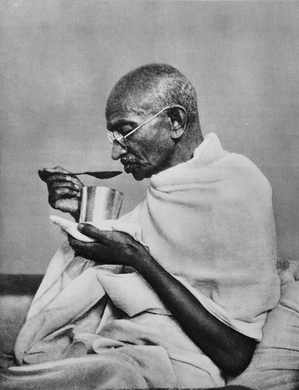 Gandhi drinking out of a cup.