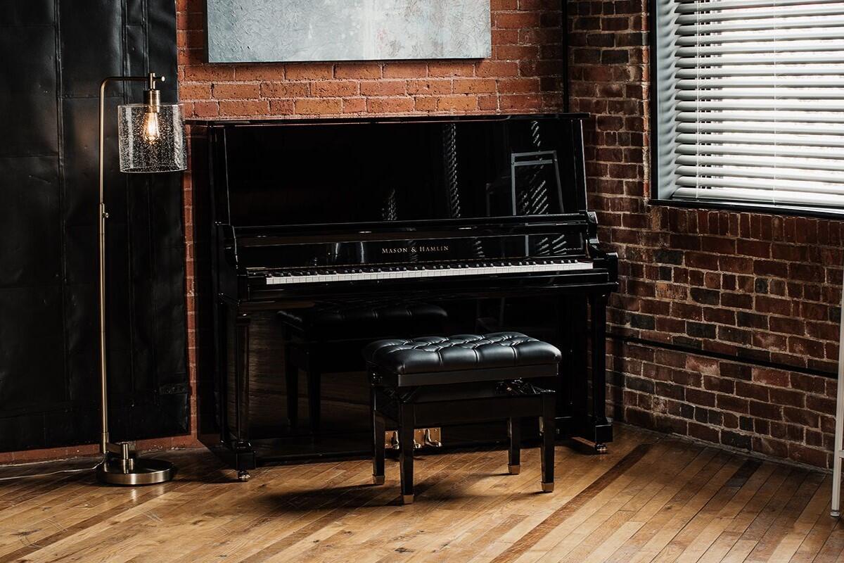 Mason and Hamlin Model 50 upright piano in a room with brick walls and wooden flooring.