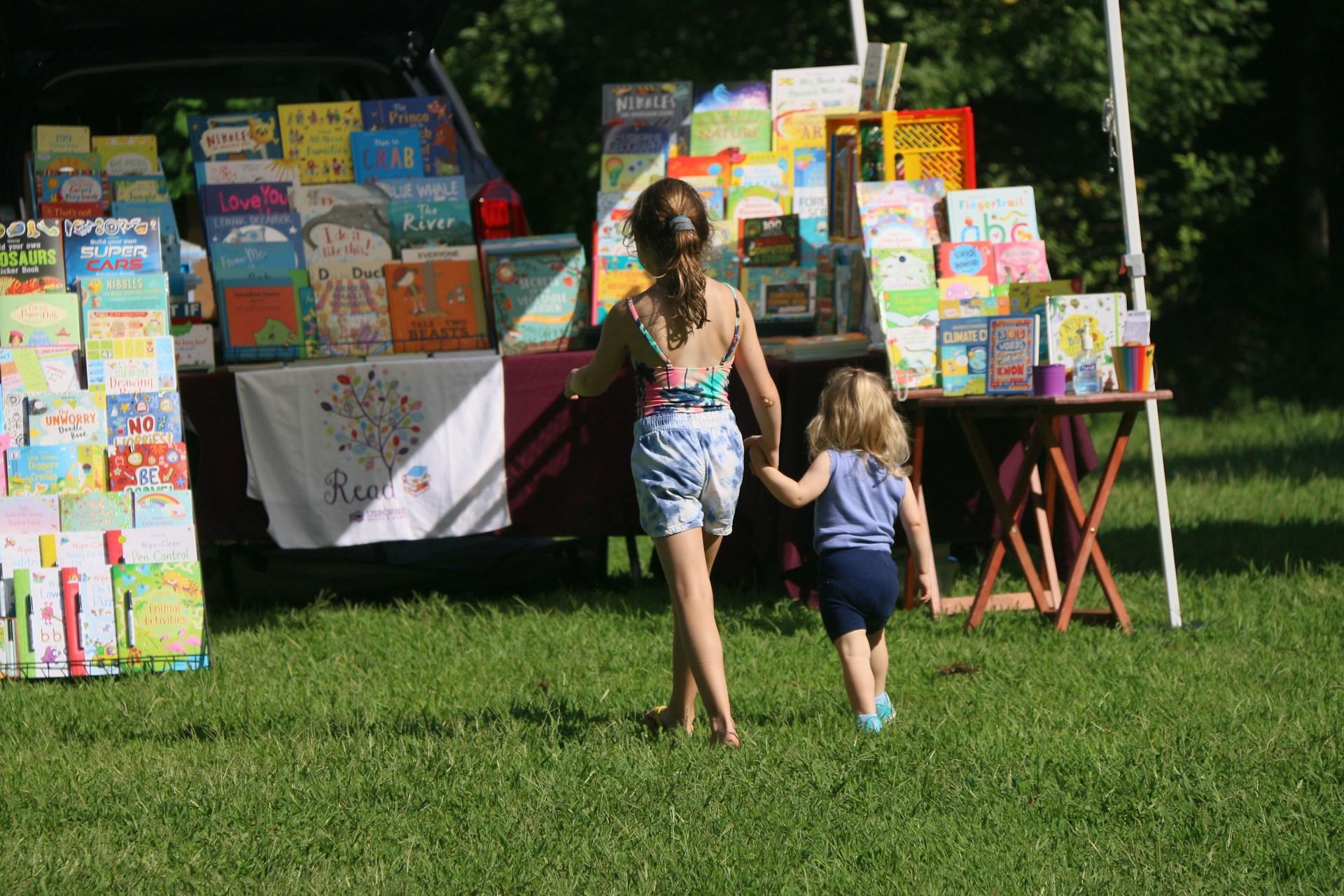 Two sisters going towards a book stand.