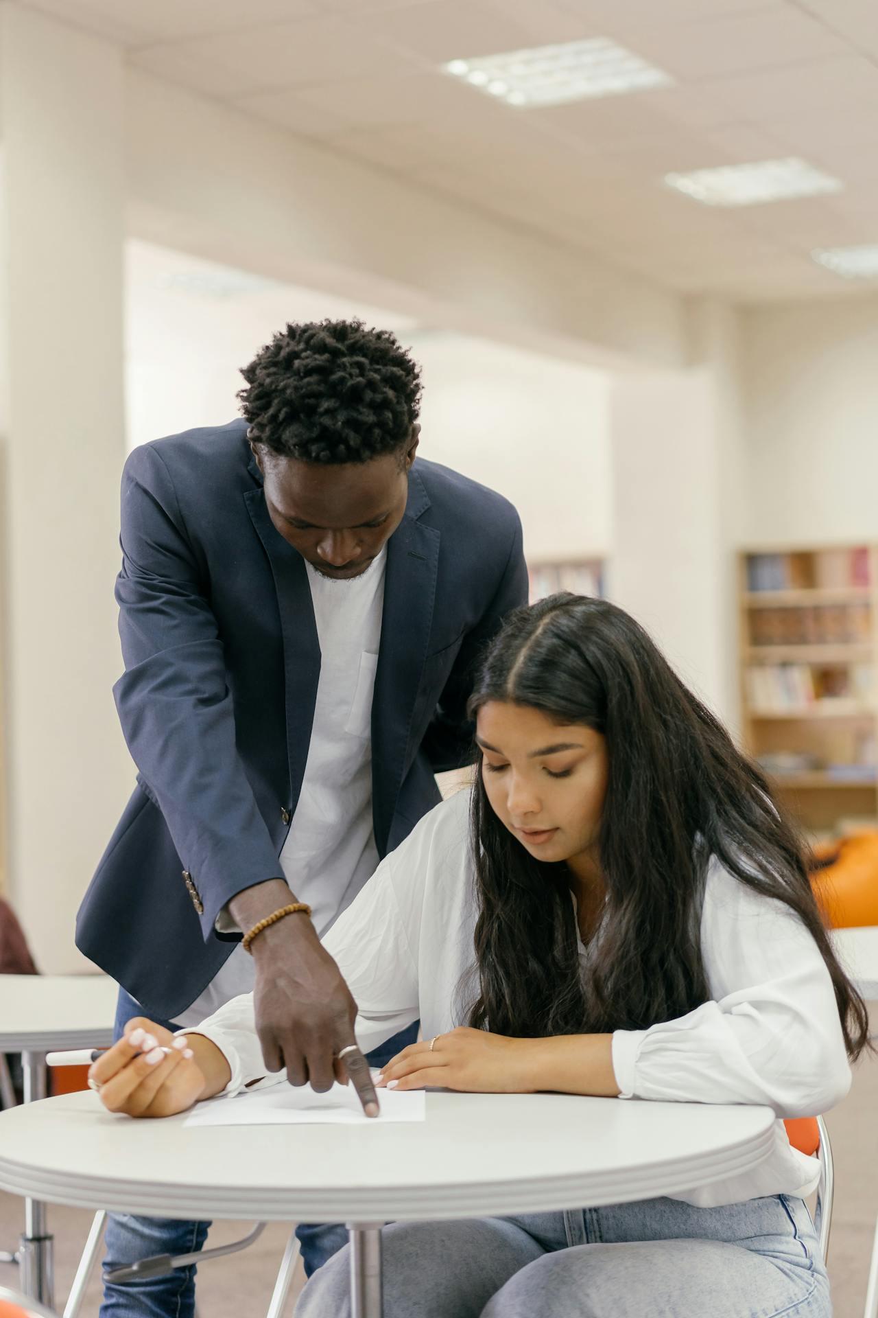 A tutor helps a student over their shoulder pointing at their work.