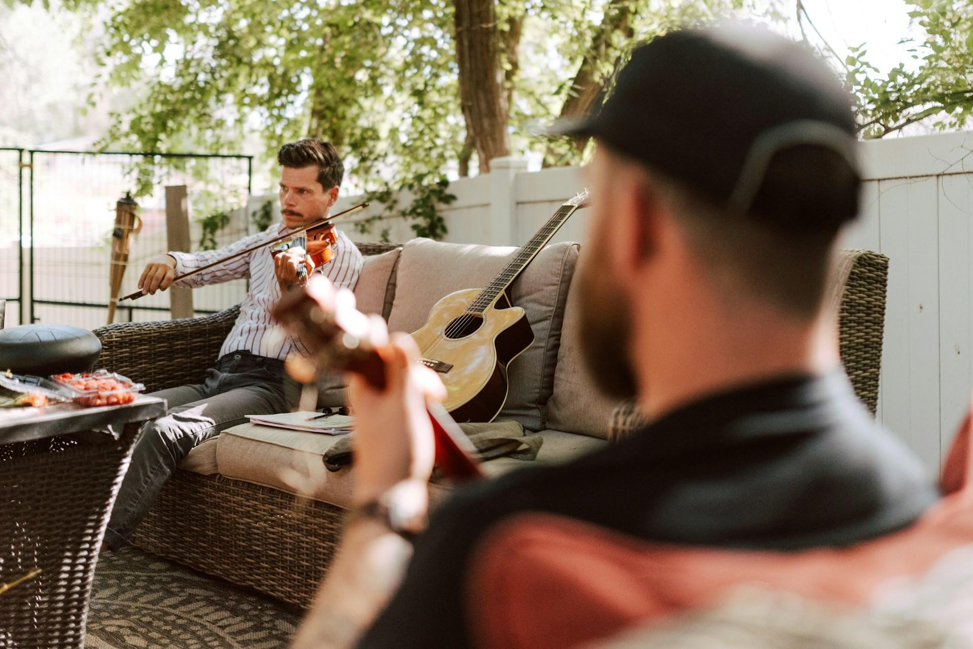 A guy playing the violin and another playing the guitar outside.